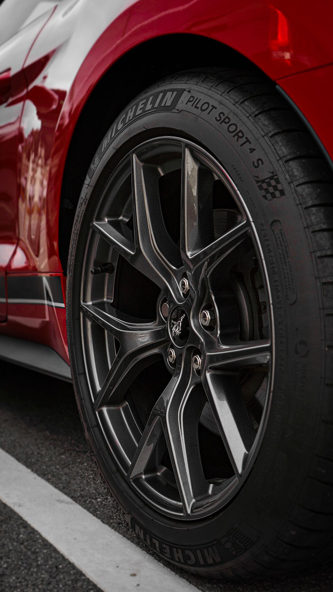 Close-up of black alloy wheels with Michelin Pilot Sport tires on a red vehicle.