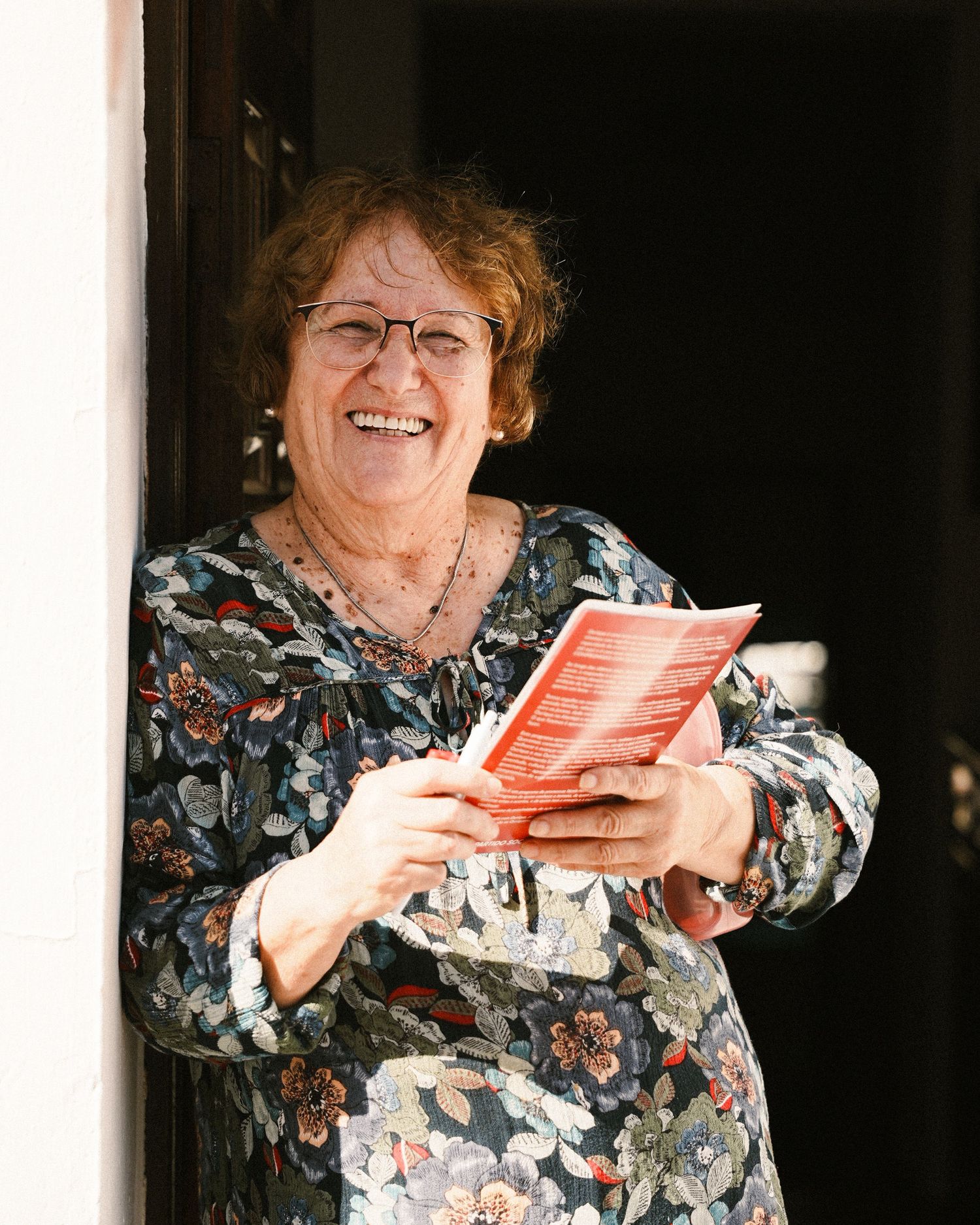 Person in floral print dress laughing while holding papers.