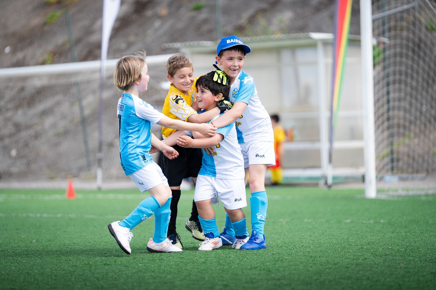 Young soccer players embrace in celebration on green turf field.
