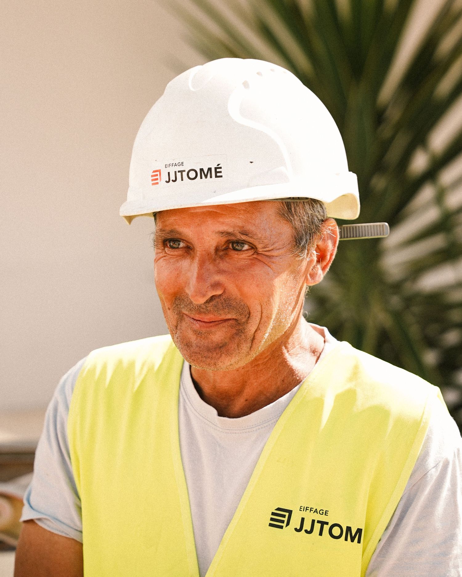 Construction worker wearing a white hard hat and yellow safety vest smiles at the camera.