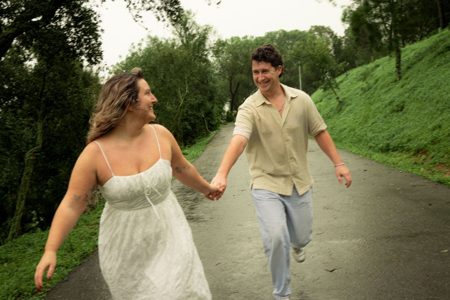 Couple holding hands and walking together on a scenic path surrounded by lush green trees and hills.