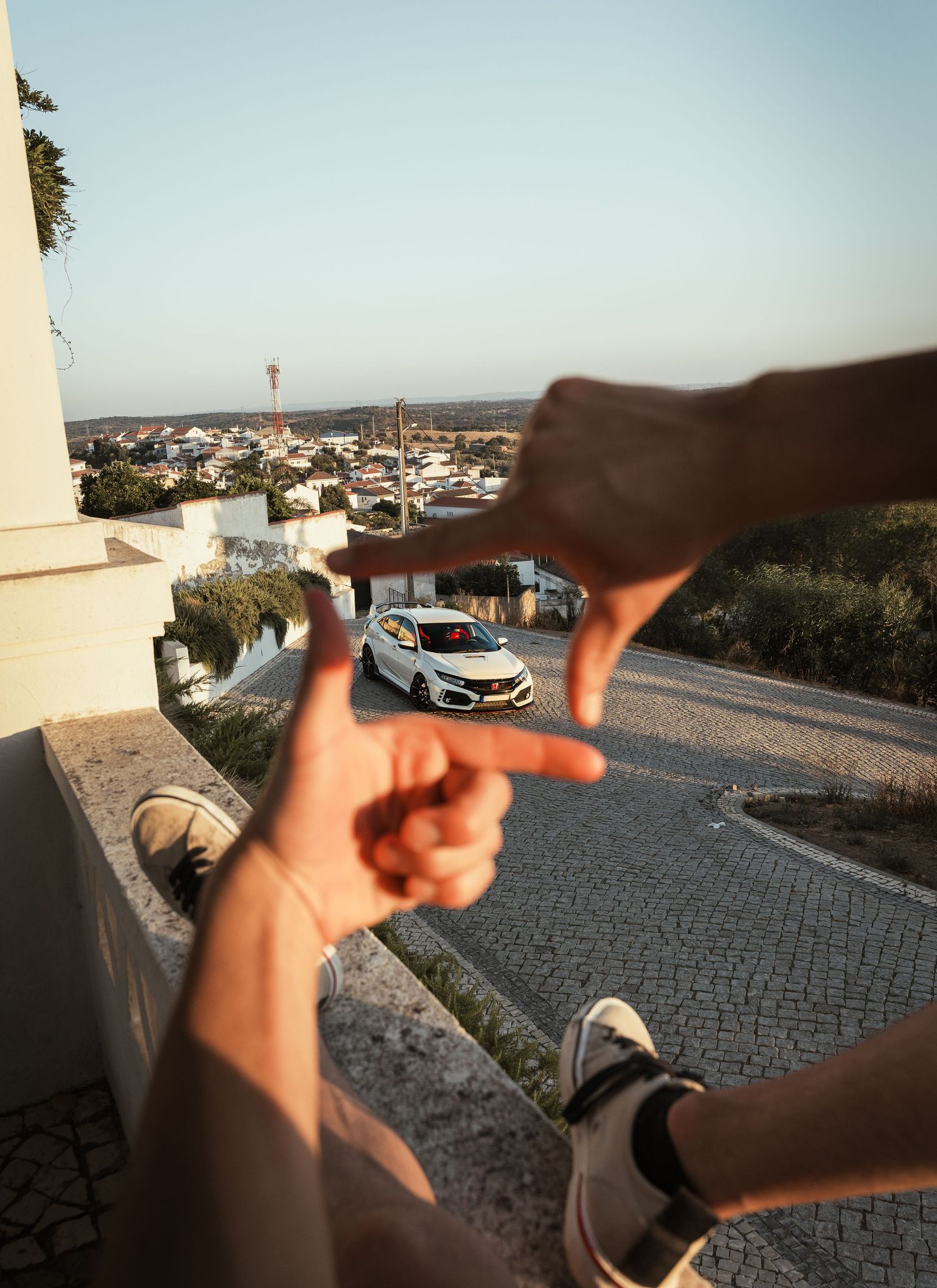 Aerial perspective of a white Honda Civic Type R parked on cobblestone with cityscape in background.