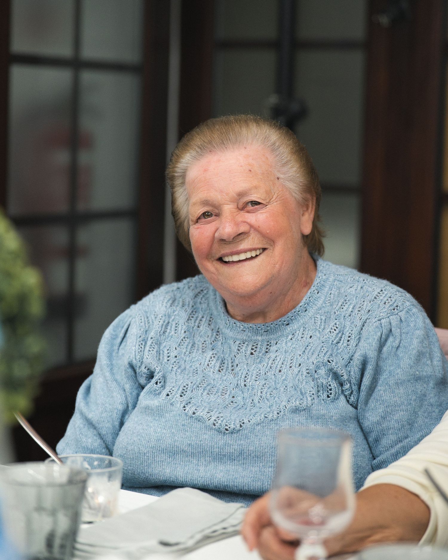 Person wearing light blue knit sweater smiling warmly at a table setting.