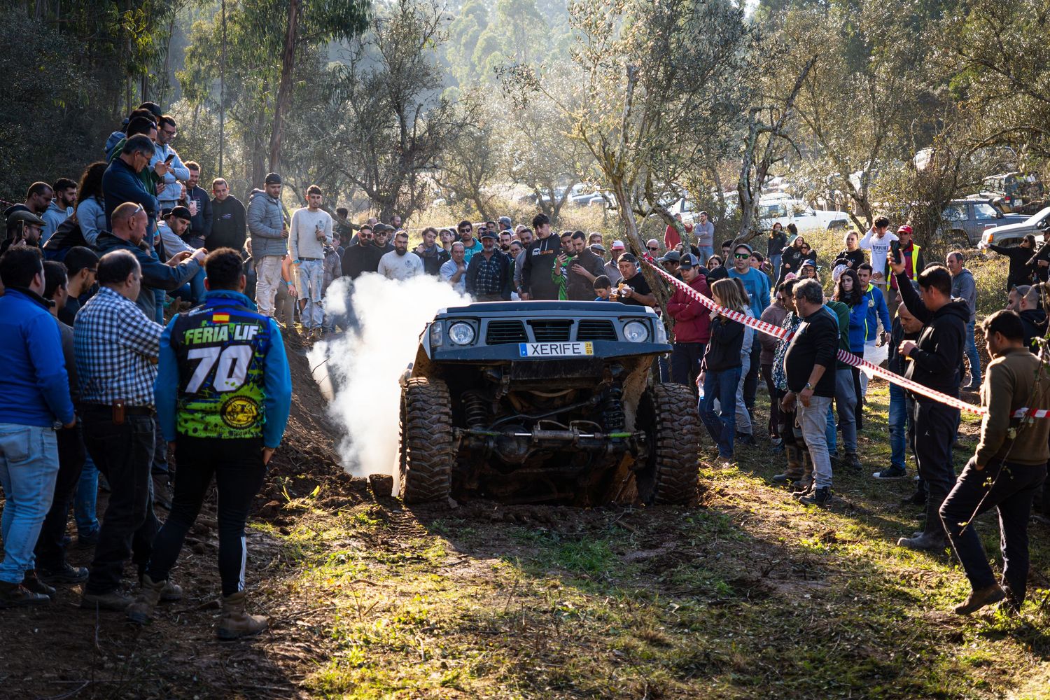 Off-road vehicle kicks up dust while performing at a crowded outdoor motorsport event with spectators watching.