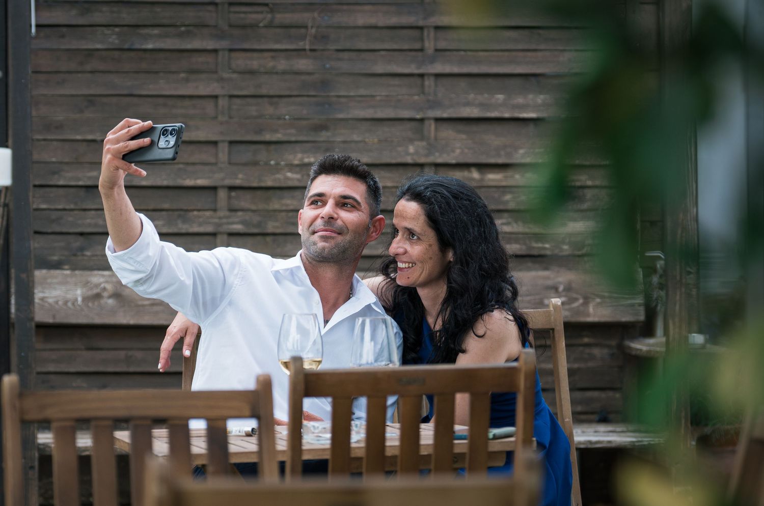 Couple taking selfie while sitting on wooden bench outdoors.