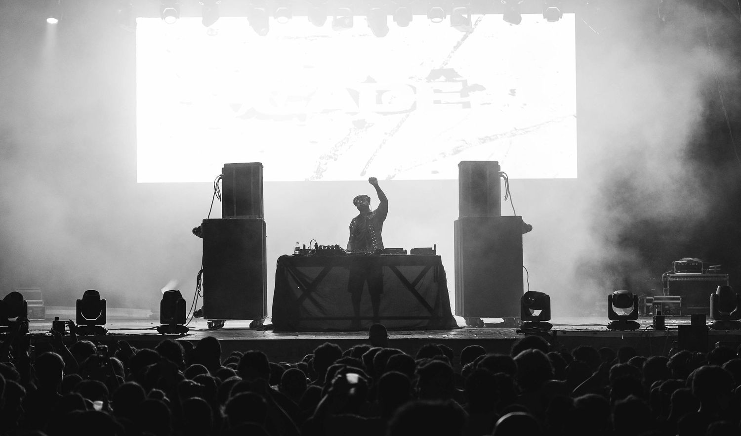 Black and white concert scene with stage equipment silhouettes and crowd in foreground.