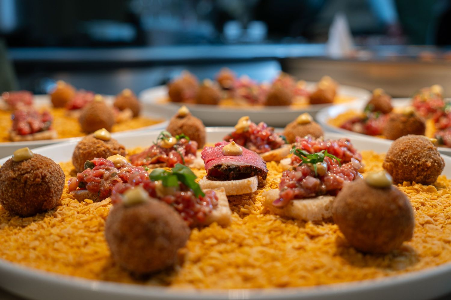 Gourmet appetizer plate with meatballs and red sauce garnished on yellow breadcrumb base.