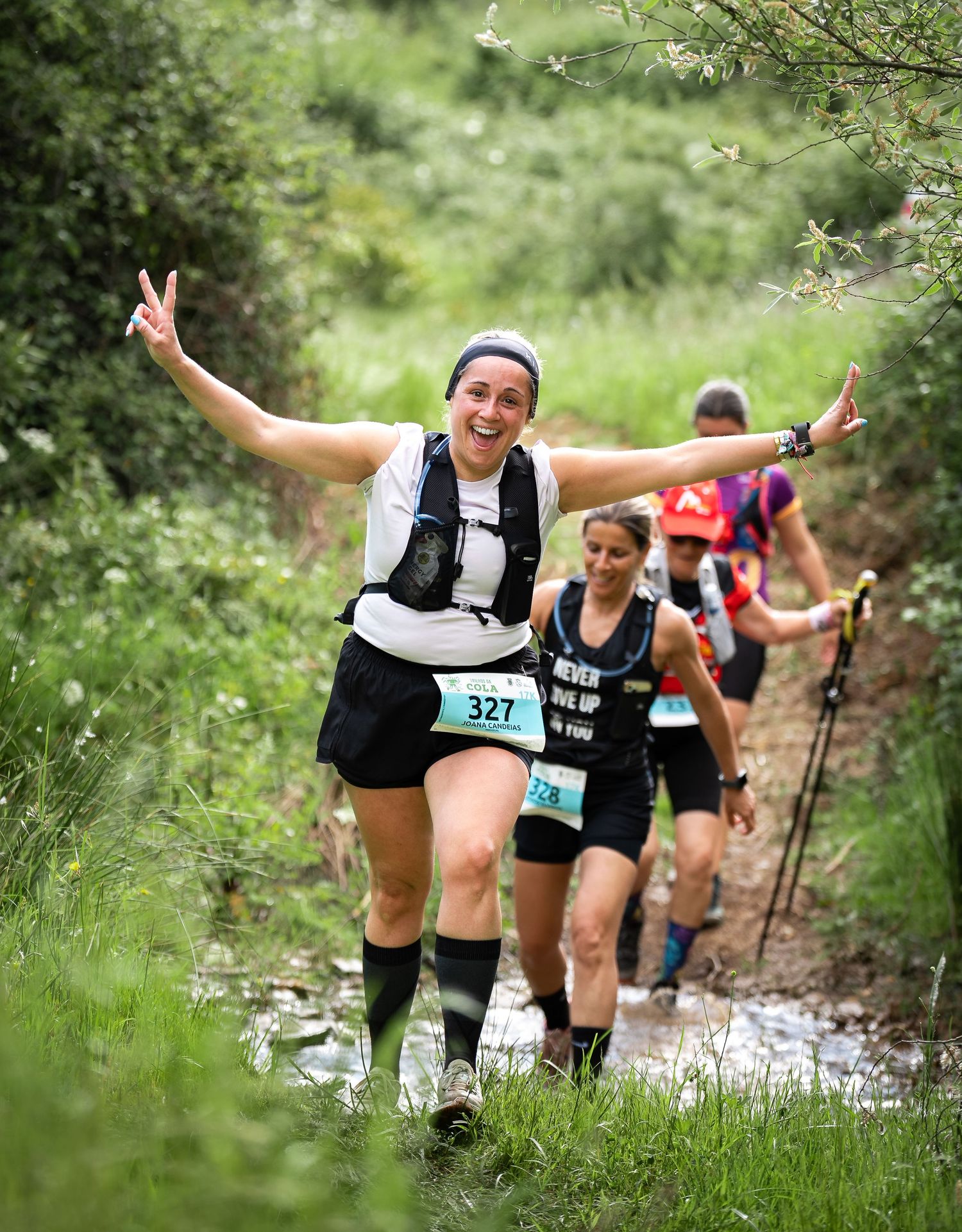 Trail runners splashing through muddy water during an outdoor race through green wilderness terrain.