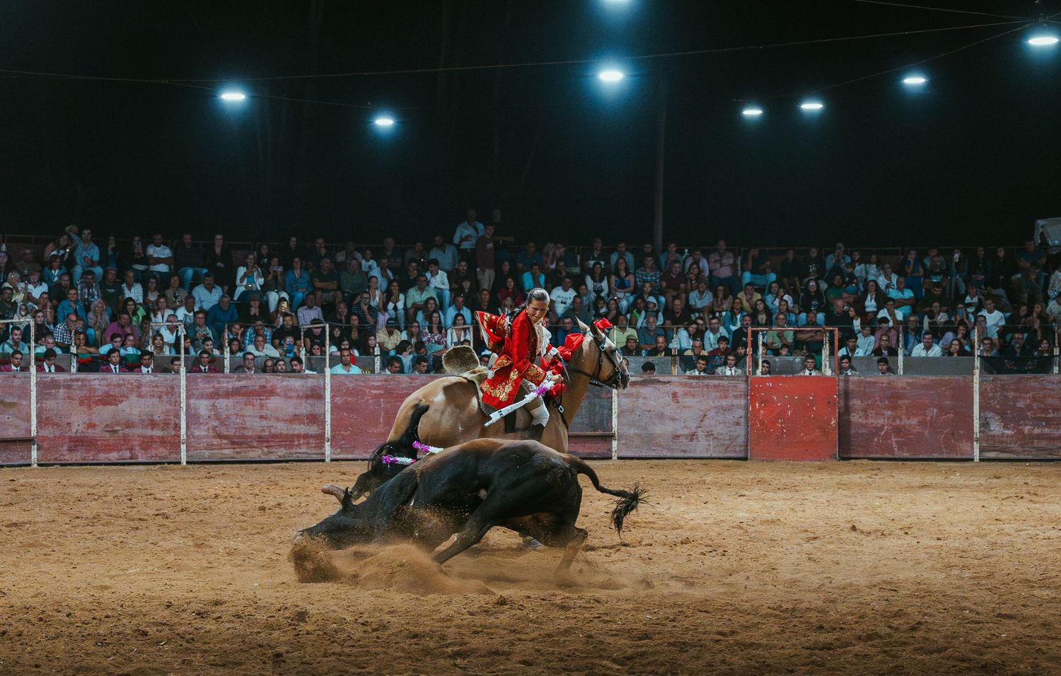 Dramatic sequence of a bull charging towards participants in a nighttime rodeo arena under bright stadium lights.