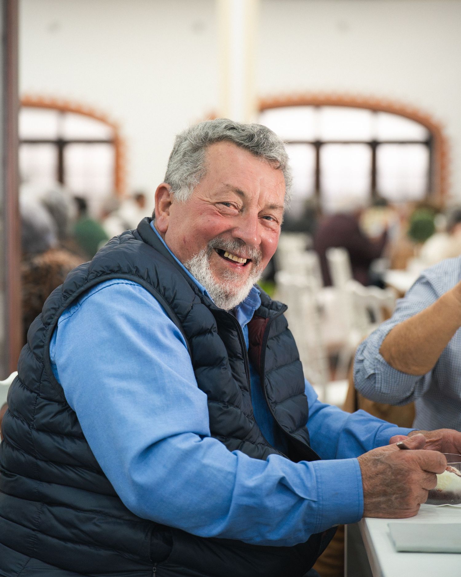Individual in light blue shirt and dark vest sharing a hearty laugh at a social event.