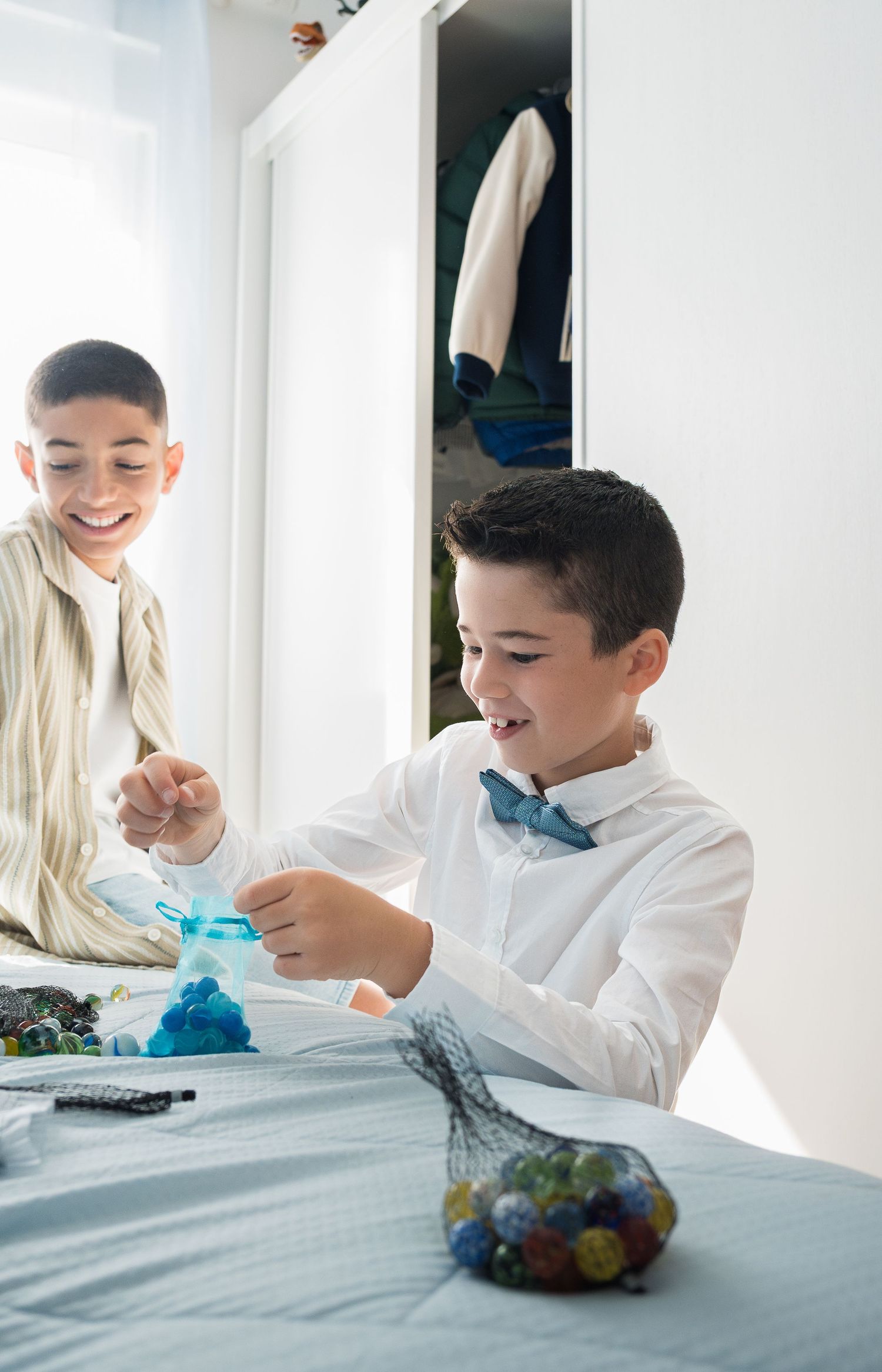 Two children playing with blue materials at table in bright room.