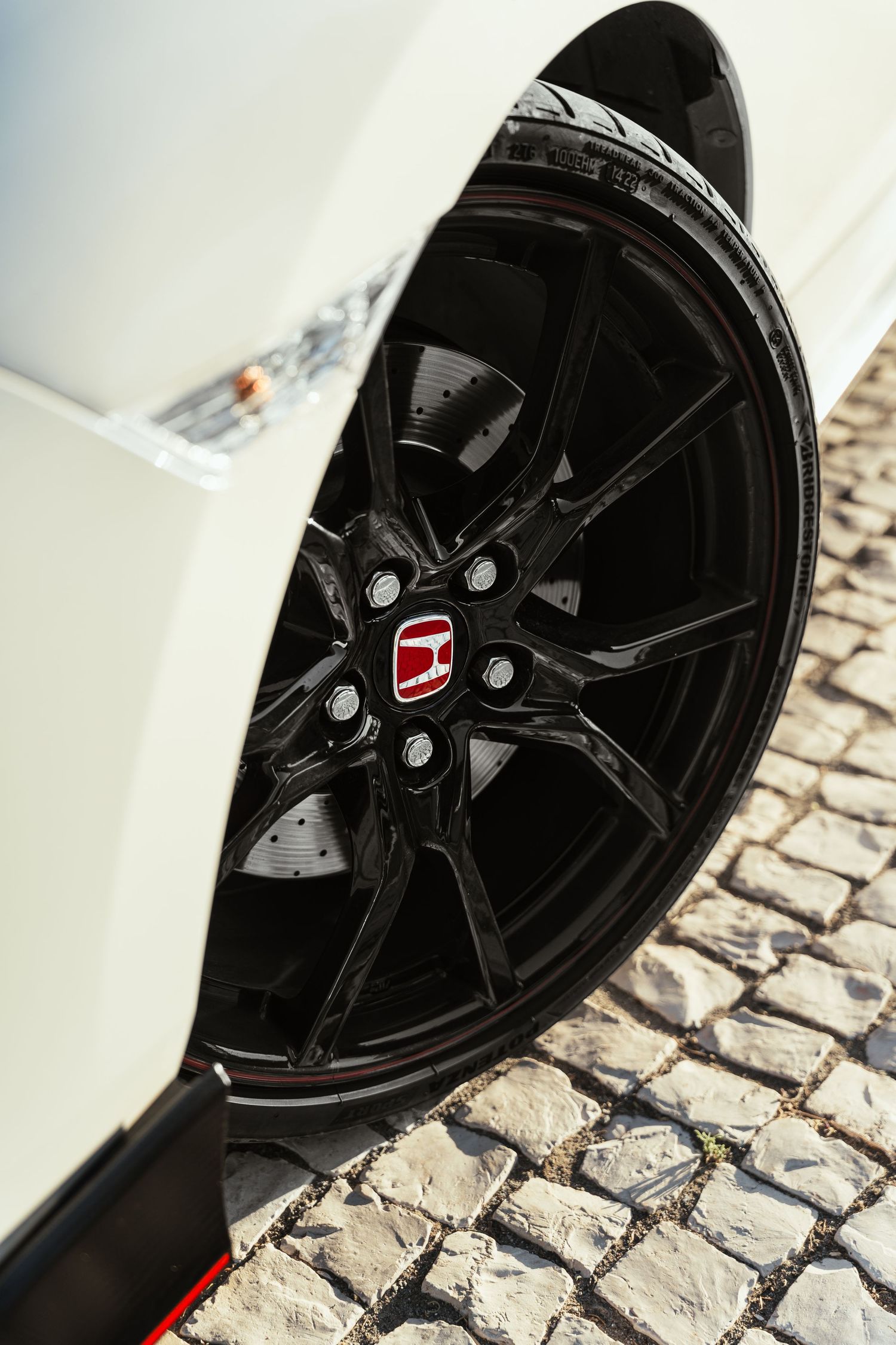 Black alloy wheel with red Honda badge detail on a white Civic Type R.