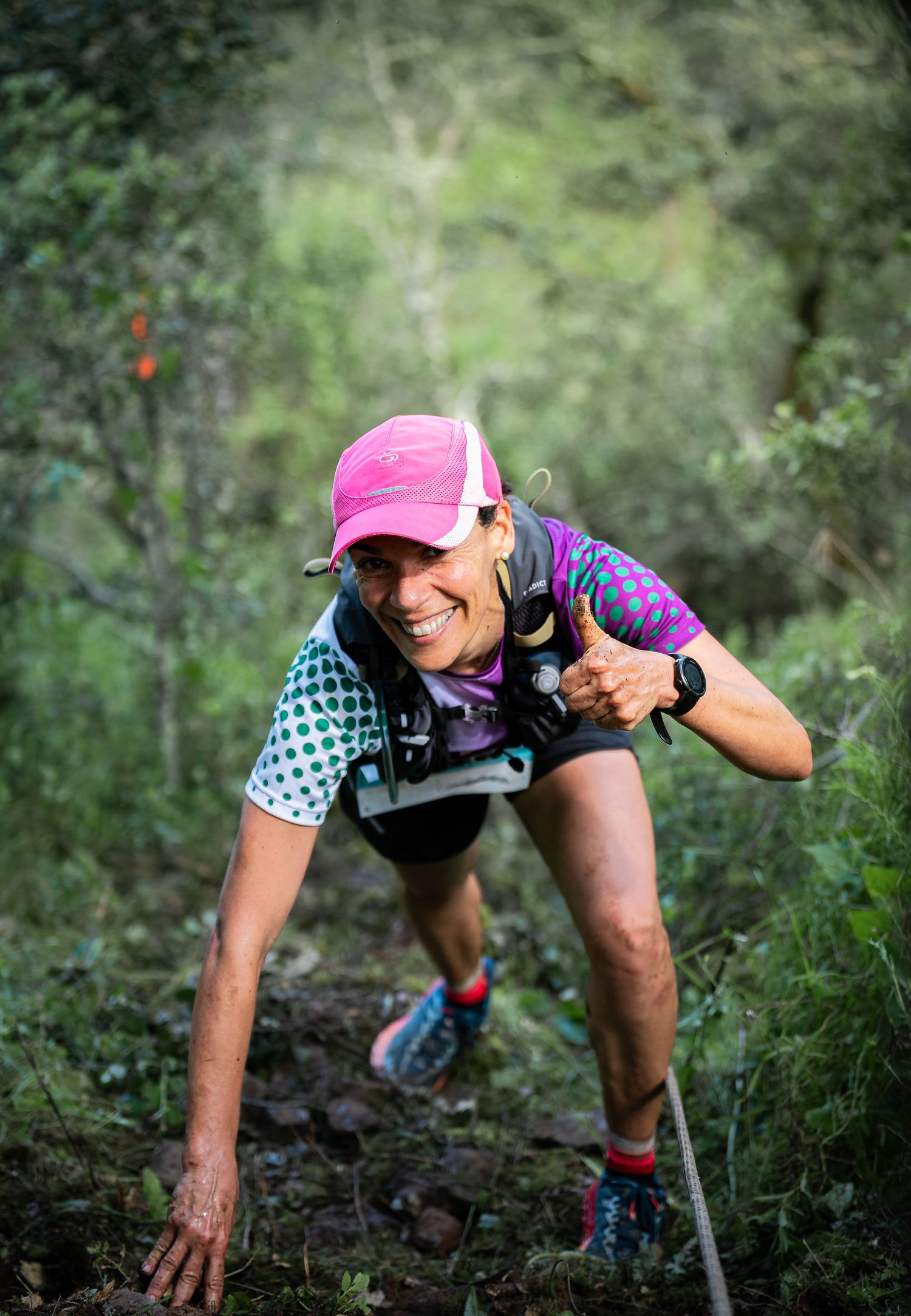 Runner in pink cap and checkered shirt climbs steep terrain using trekking poles.