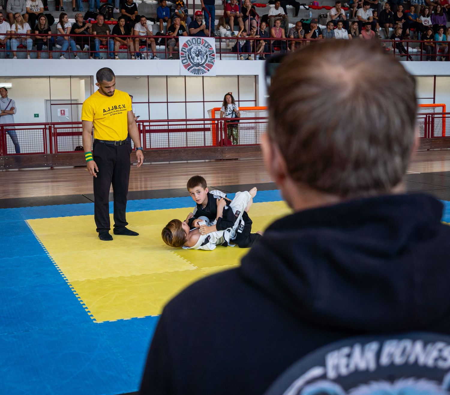 Martial arts competitors grappling during a tournament match on blue and yellow mats.