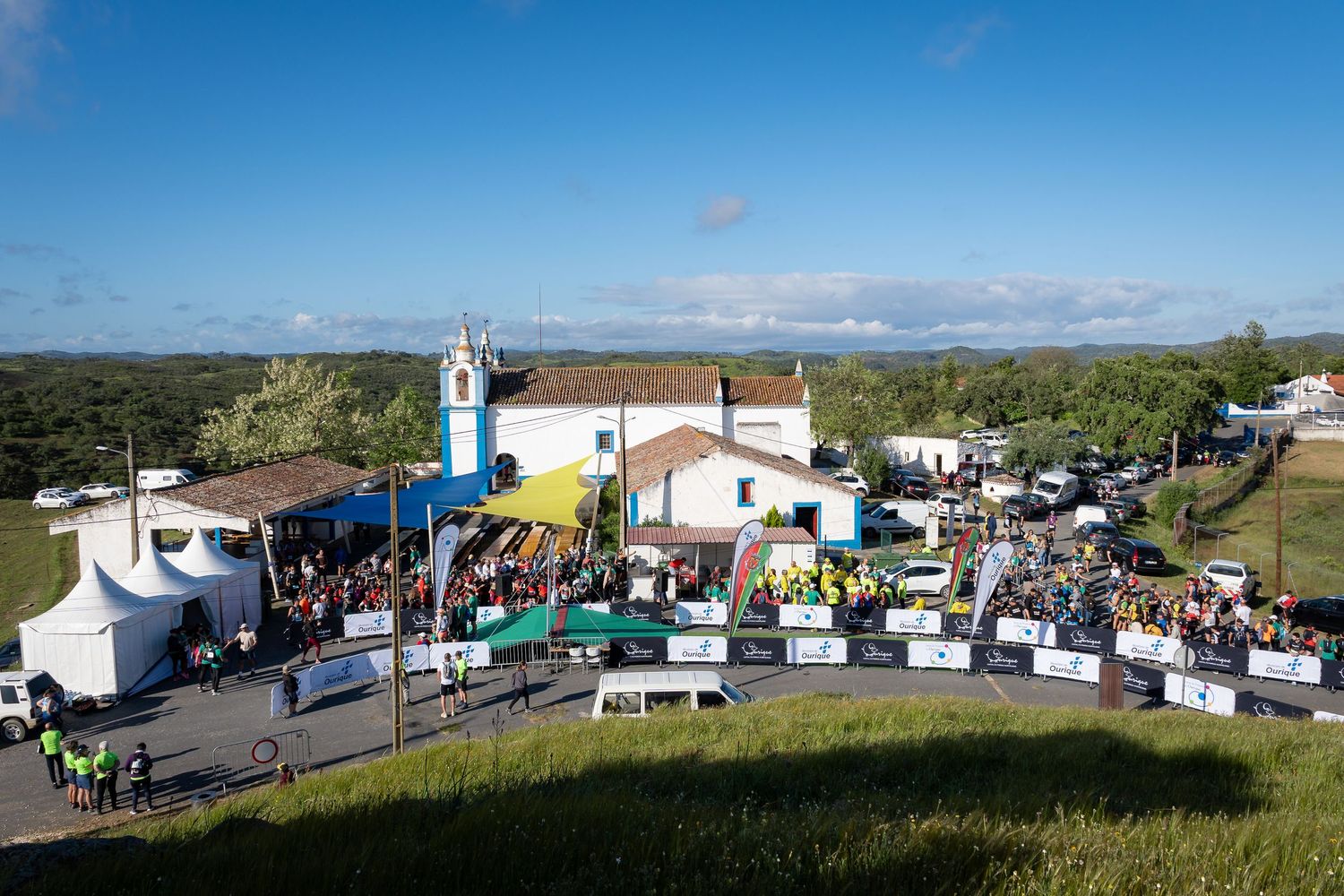 Aerial view of outdoor event venue with white tents and church building surrounded by crowds.