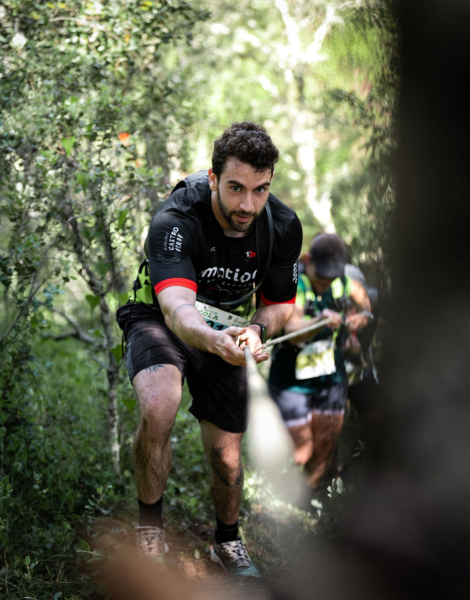 Runner in black athletic gear climbs steep forest trail during competition.