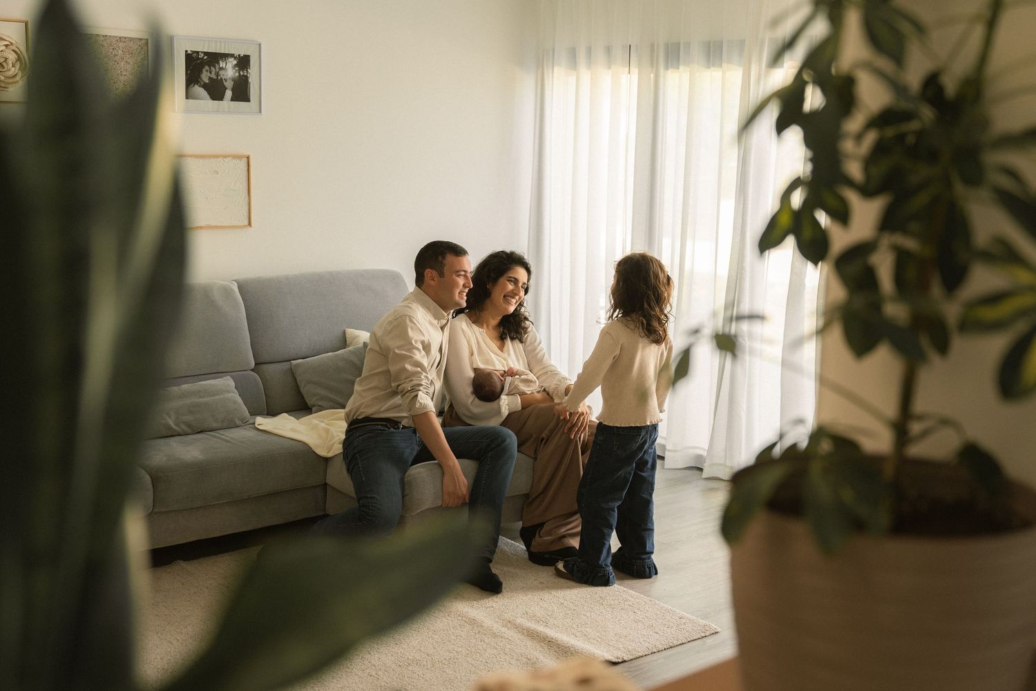 Happy family with two parents and a child bonding together in a bright, cozy living room near a gray sofa.