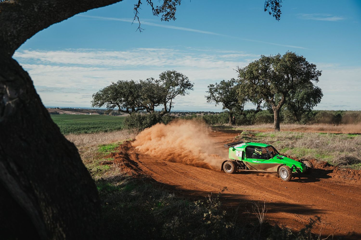 Wide landscape shot of a racing buggy creating dust trails on a rural dirt course.