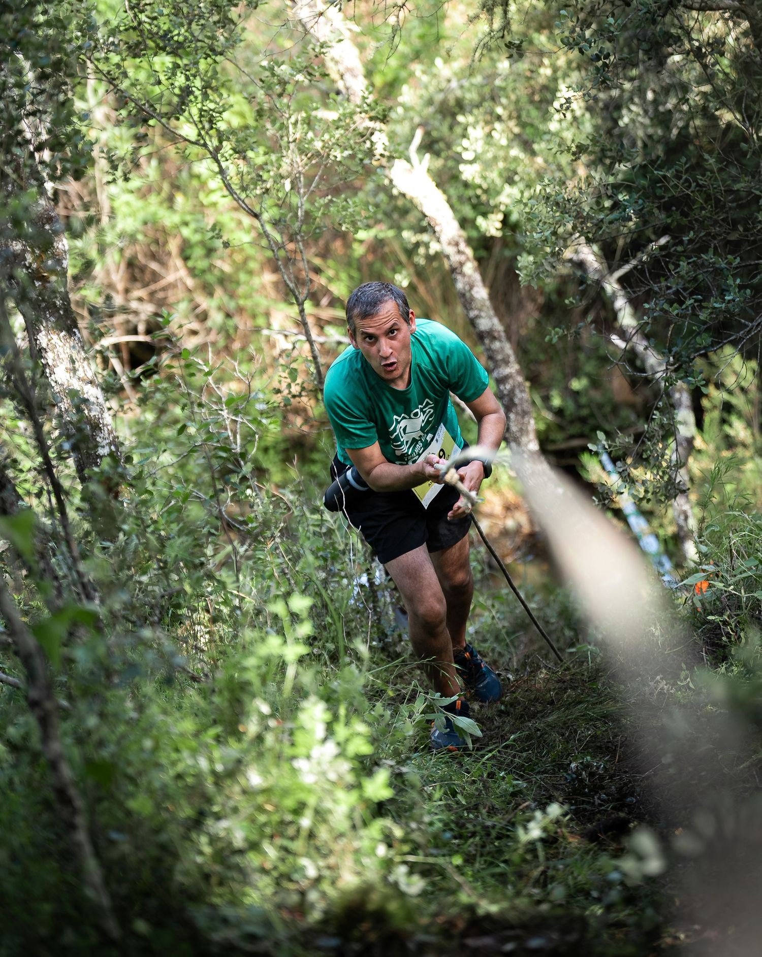 Runner in green shirt climbing steep forest trail during competitive race.