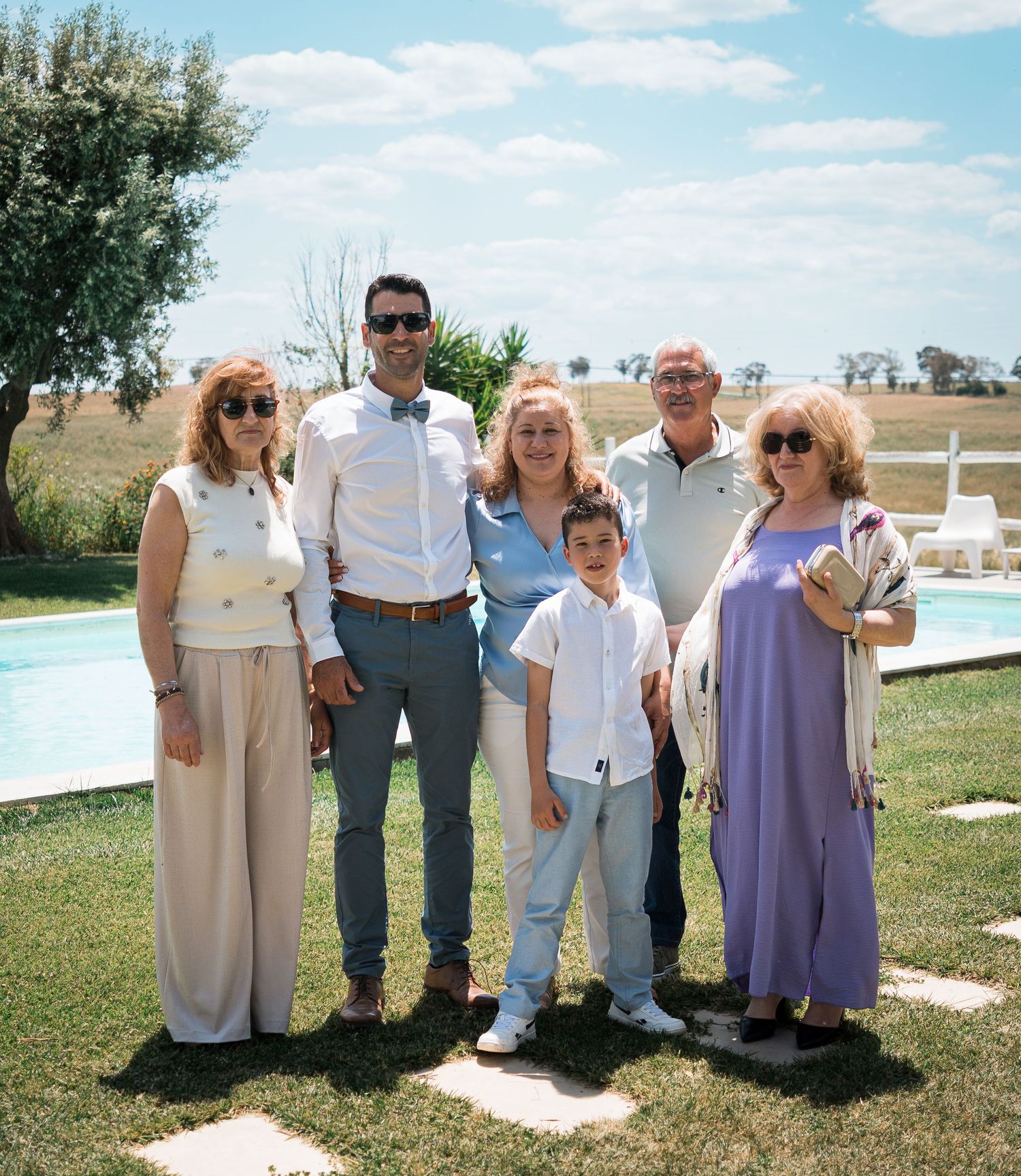 Group photo of wedding guests in coordinated outfits standing on grass near a pool.