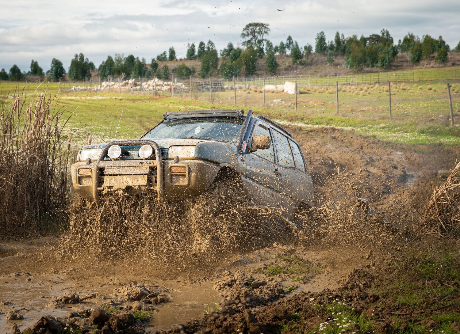 A muddy off-road vehicle splashes through deep puddles and dirt on a challenging 4x4 trail course.