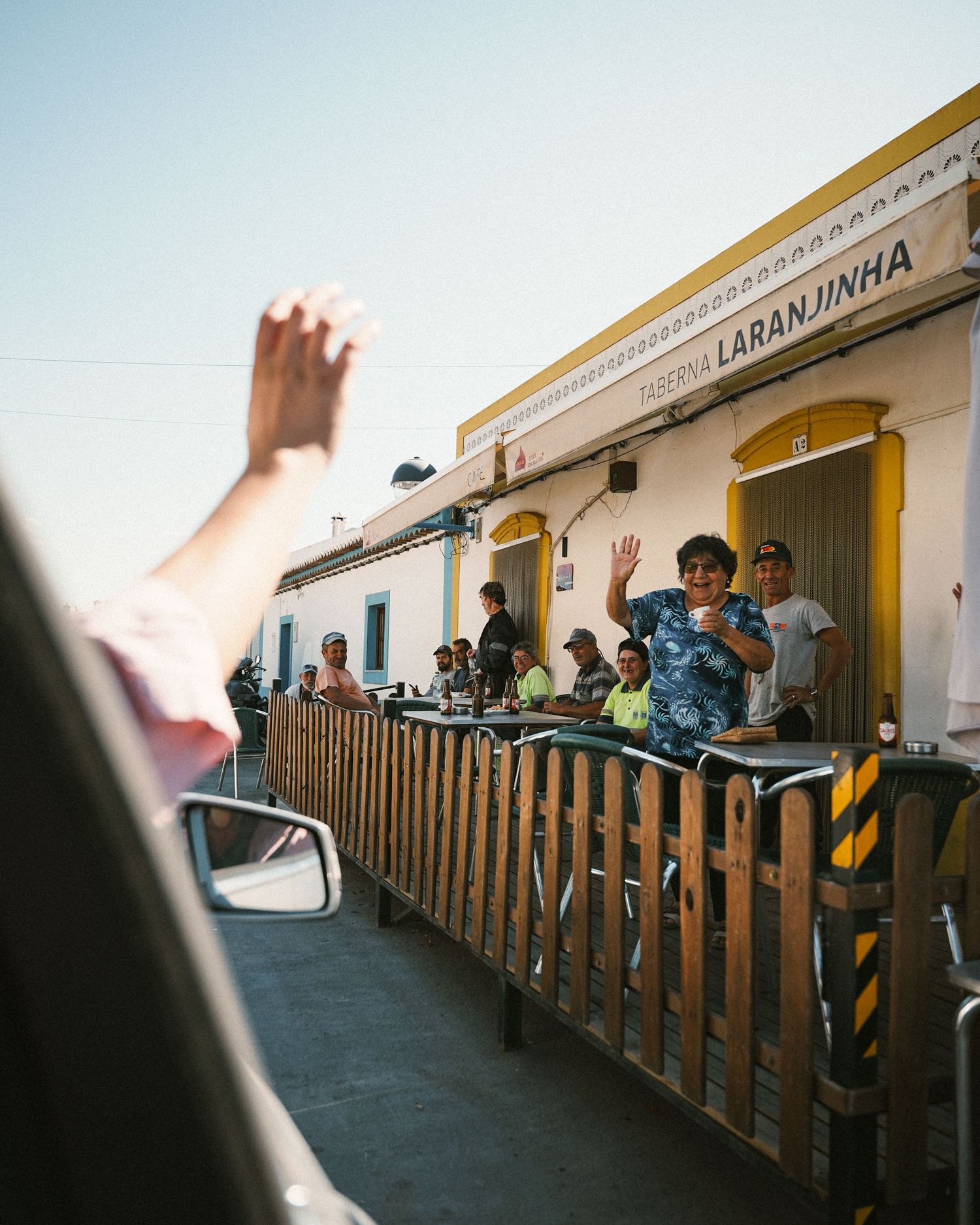 People sit along a wooden railing outside a building with yellow trim.