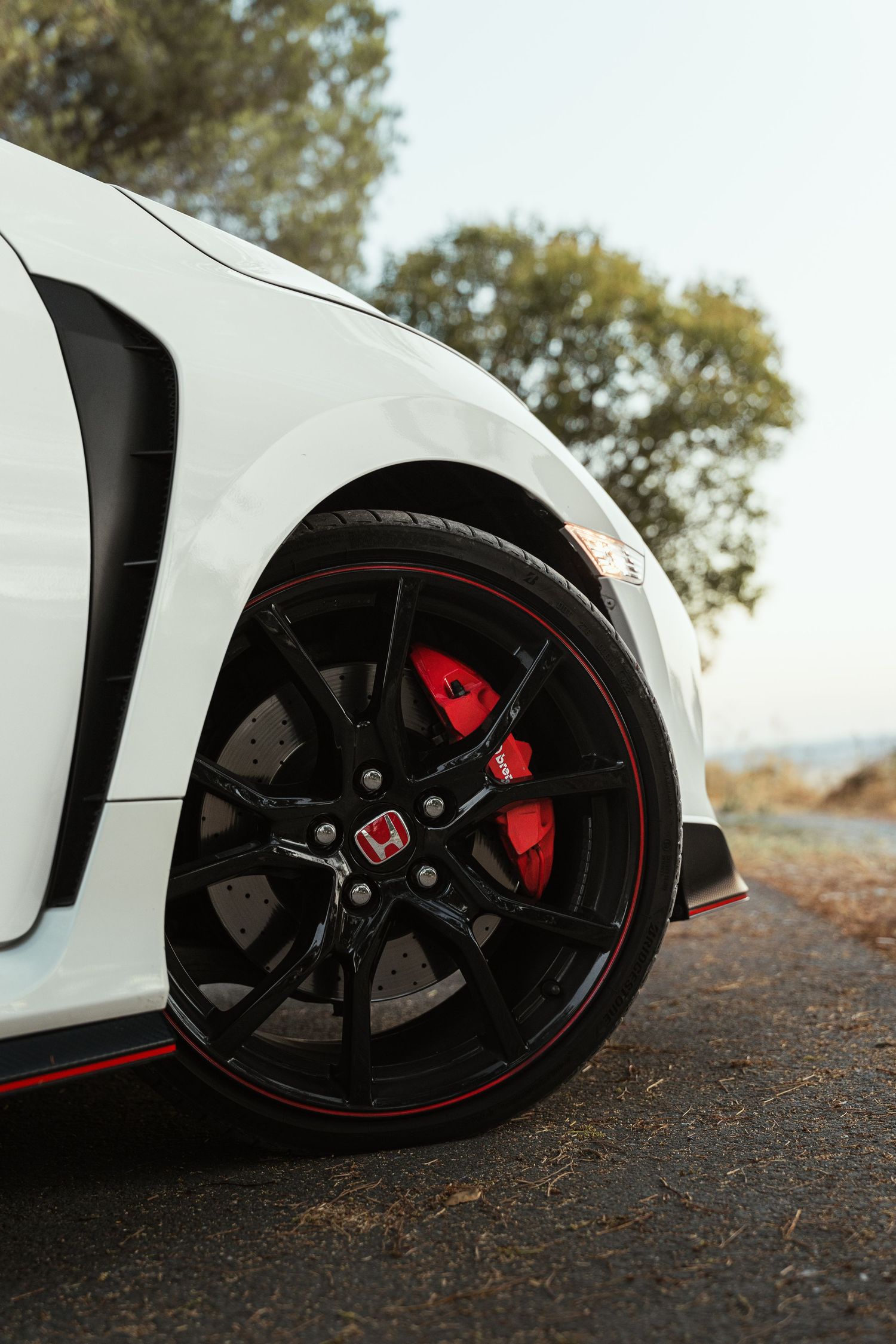 Black wheels with red brake calipers on a lowered white Honda Civic.