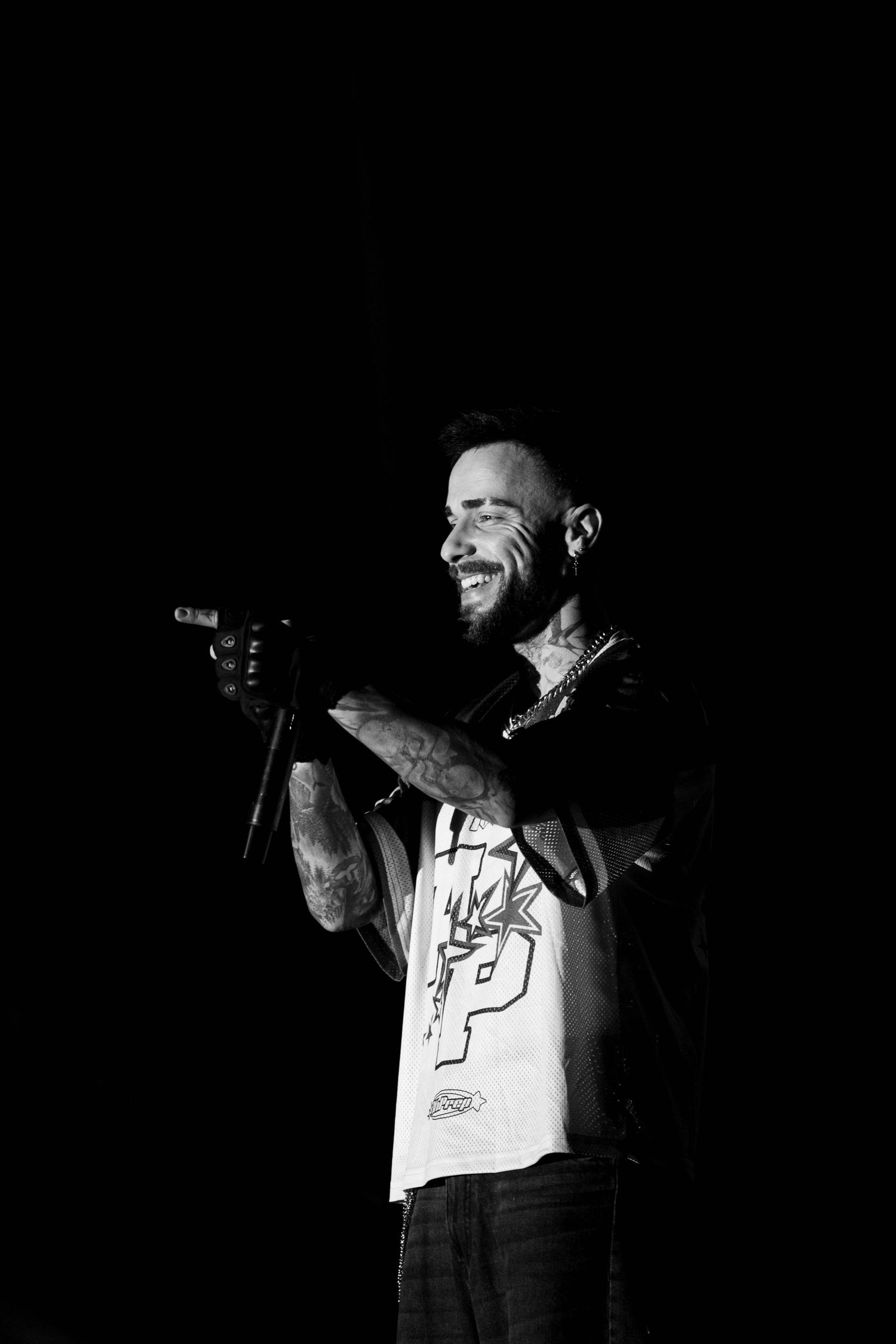Performer in white t-shirt singing on dark stage with dramatic lighting.