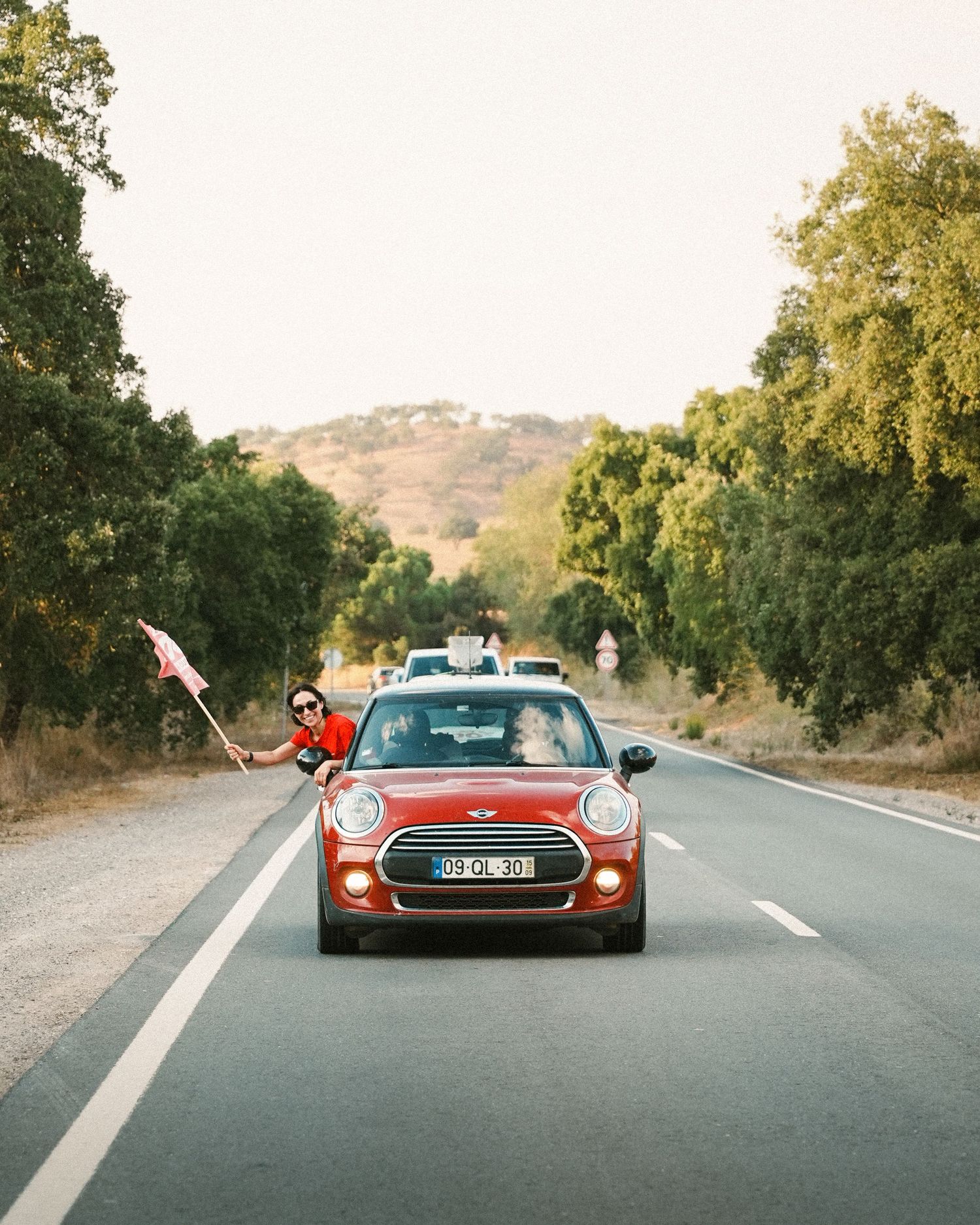 Sports cars driving on a scenic mountain road lined with oak trees.