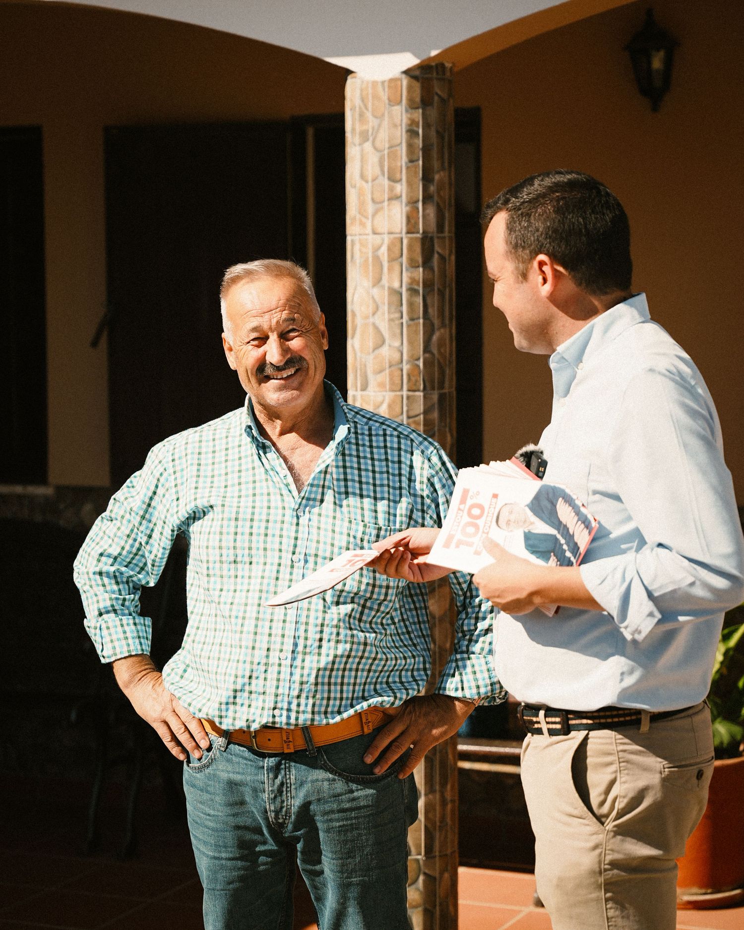 Two people having a friendly conversation on a porch with stone columns.