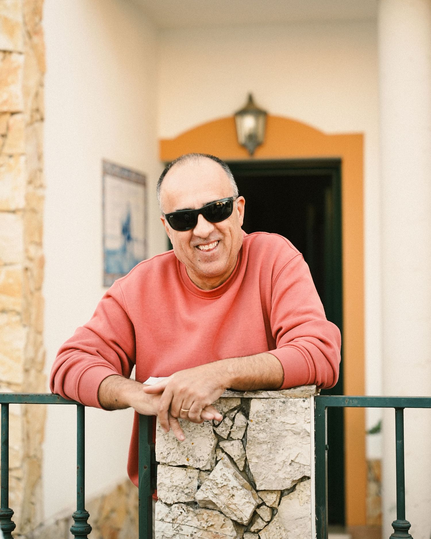 Someone in a pink sweater and sunglasses leans on a stone wall outside a building.