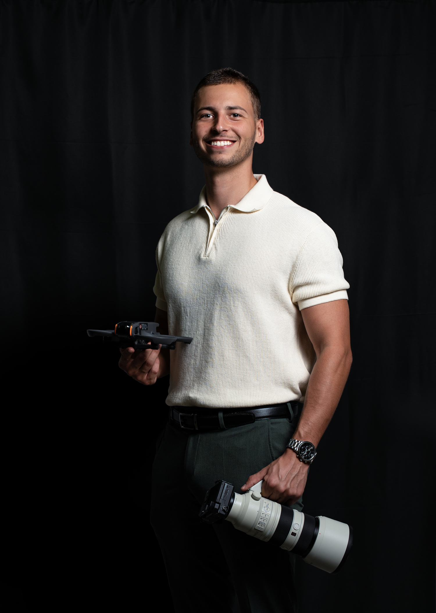 Photographer holding professional camera equipment against dark studio background.