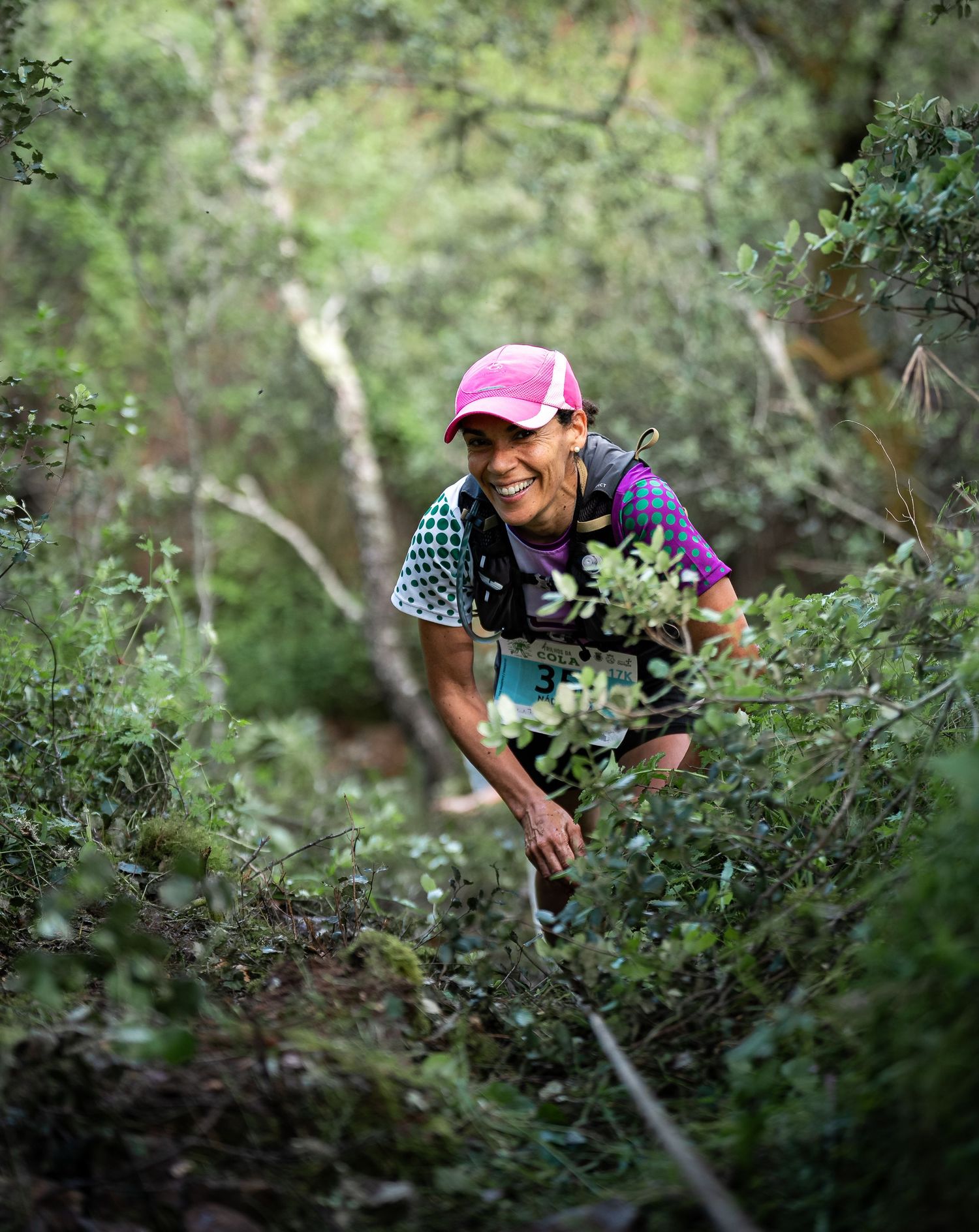 Trail runner with trekking poles navigates through dense forest vegetation.