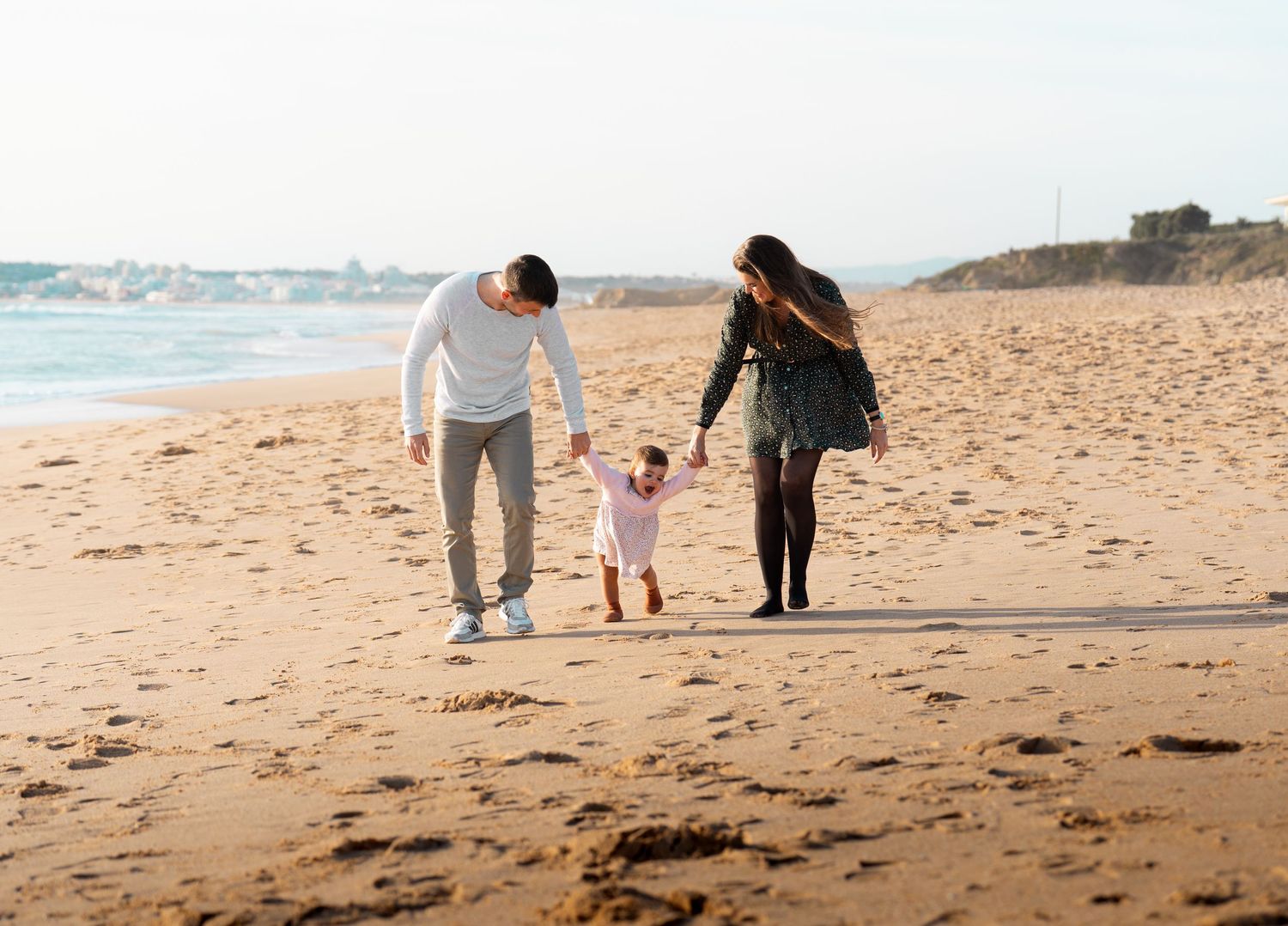 People walk along a scenic sandy beach with ocean waves in the distance.