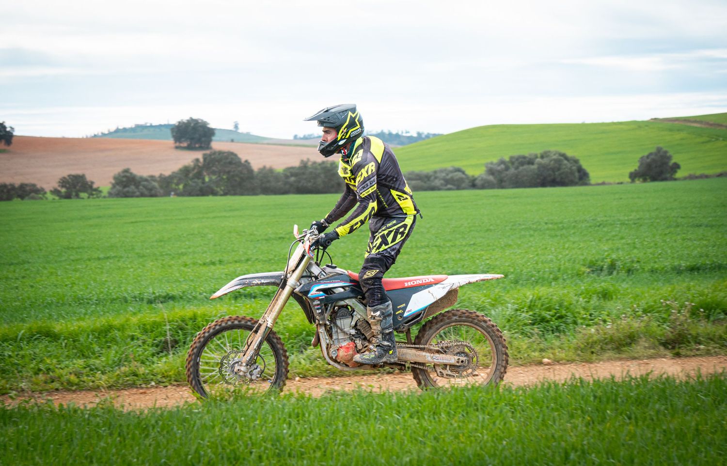 A row of dirt bikes parked on green rolling hills against a cloudy sky during an off-road adventure.