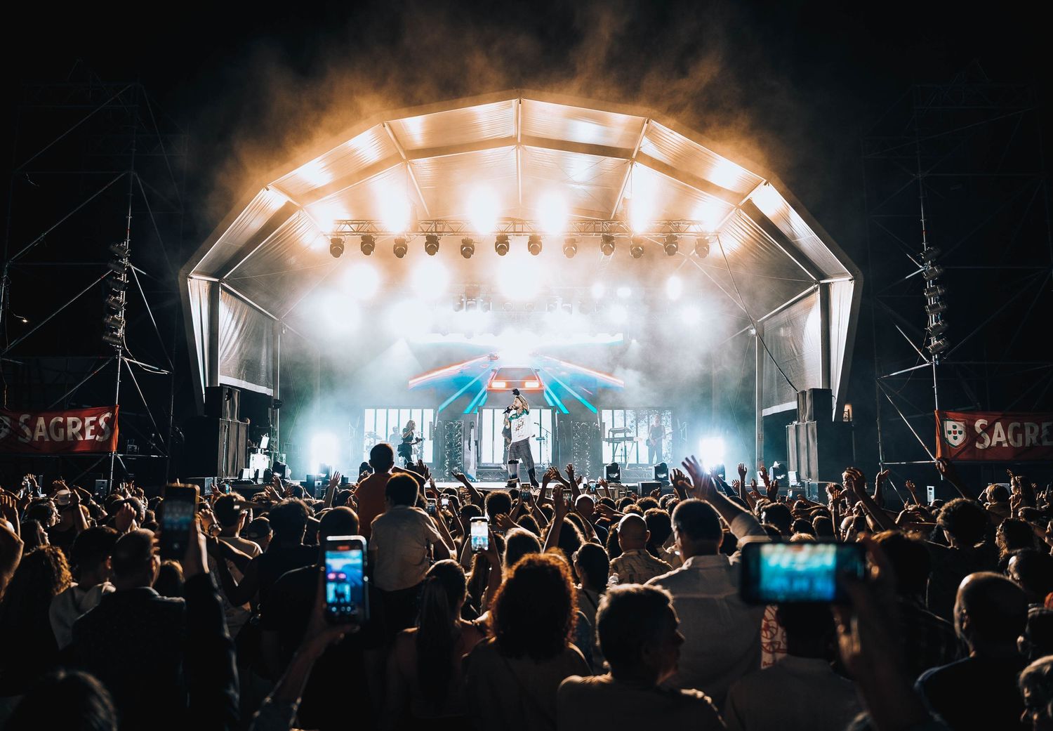 Wide panoramic view of concert stage with dramatic lighting and crowd silhouettes in foreground.