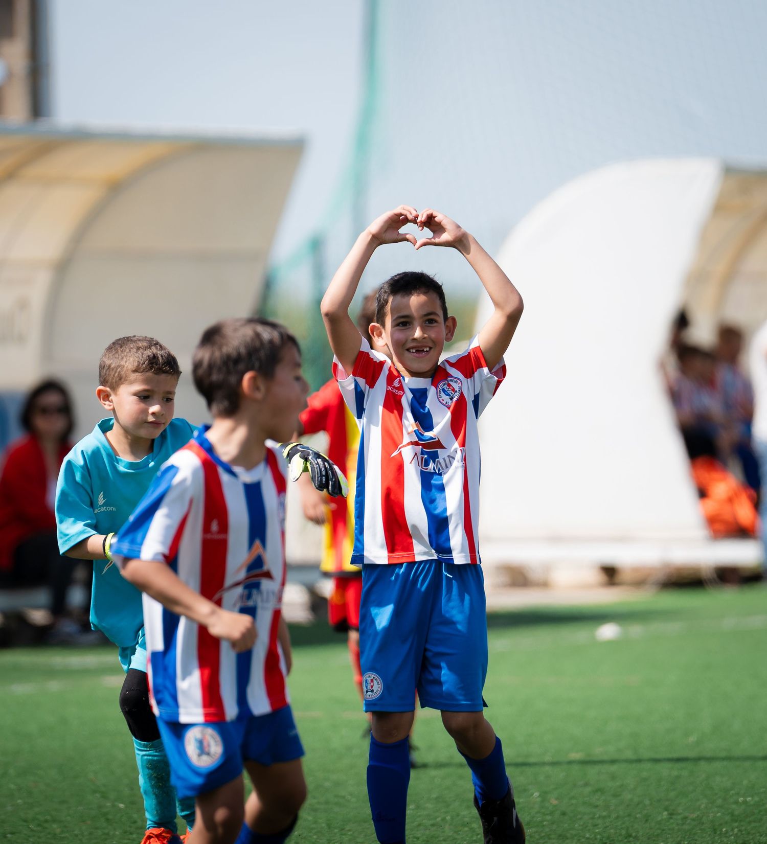 Young player makes heart gesture while celebrating on soccer field.
