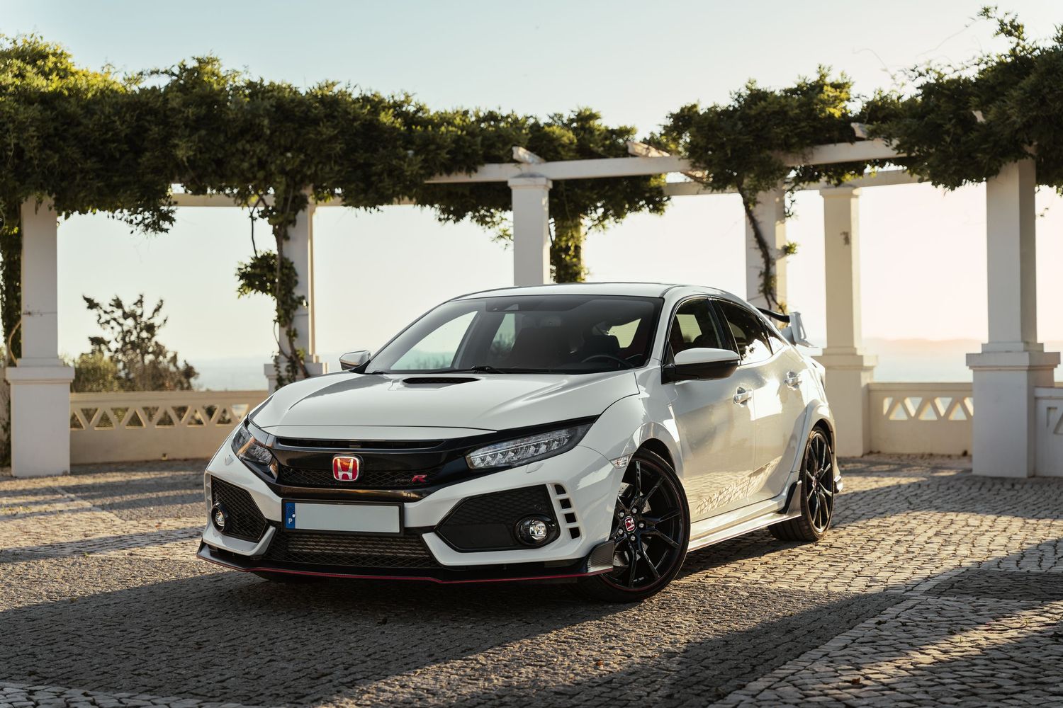White Honda Civic Type R parked in front of white columns on cobblestone pavement.