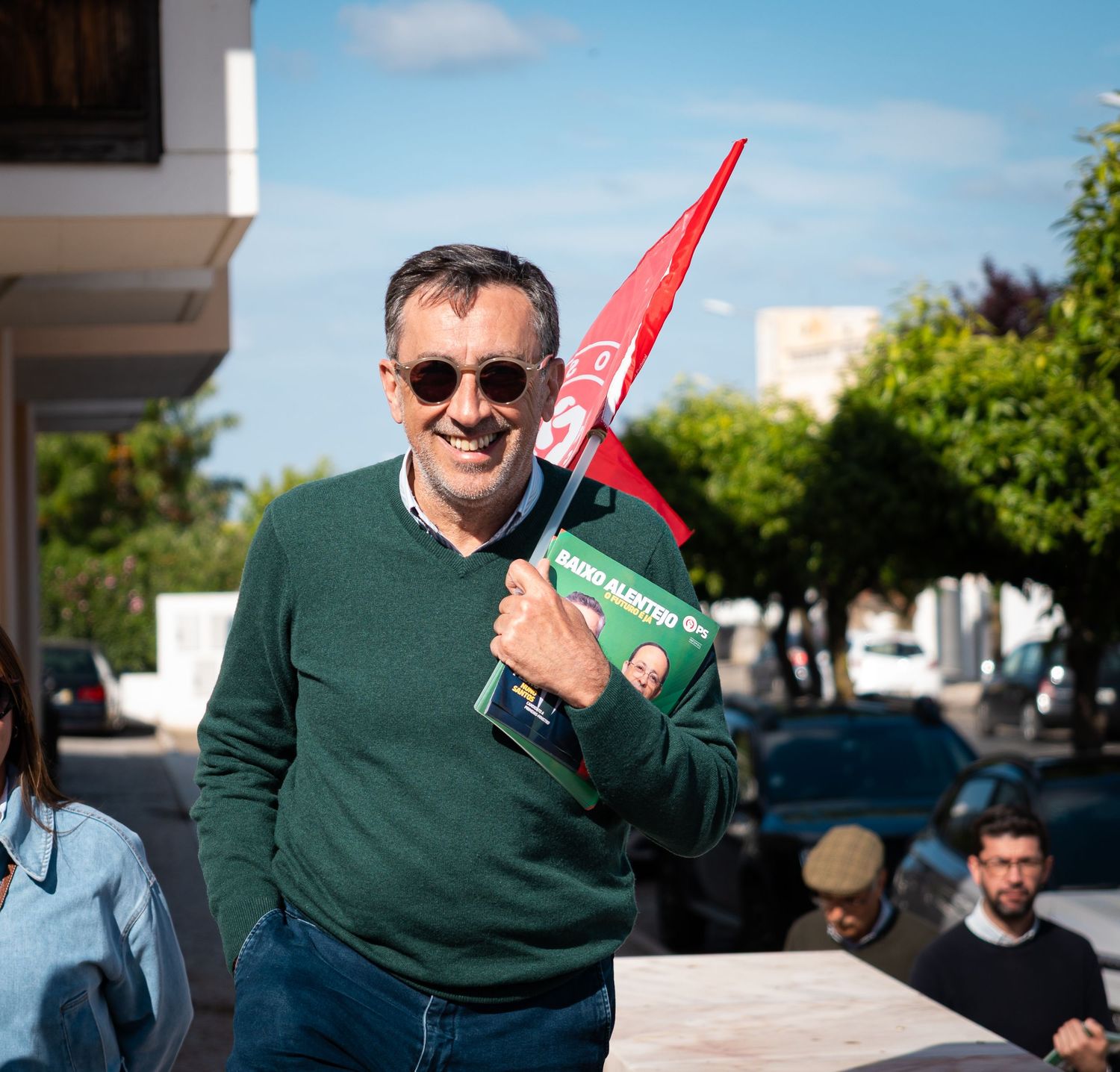 Person in green sweater waving with red flags against blue sky background.