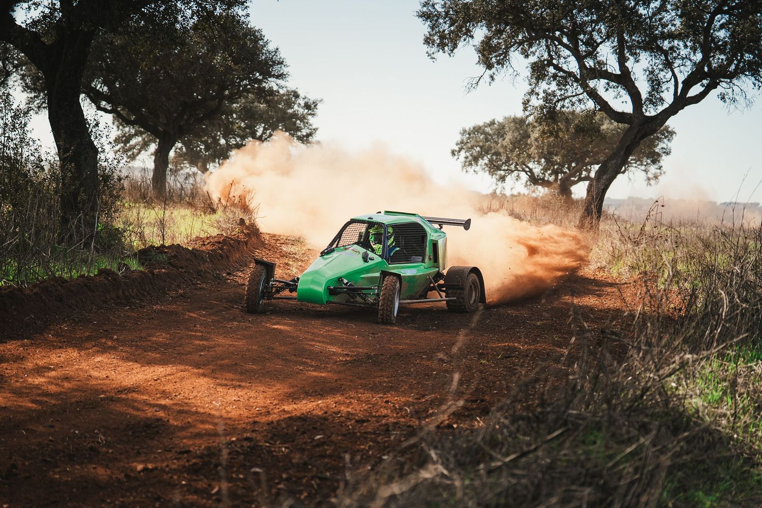 Green off-road buggy drifting around a dusty corner on a challenging dirt track.