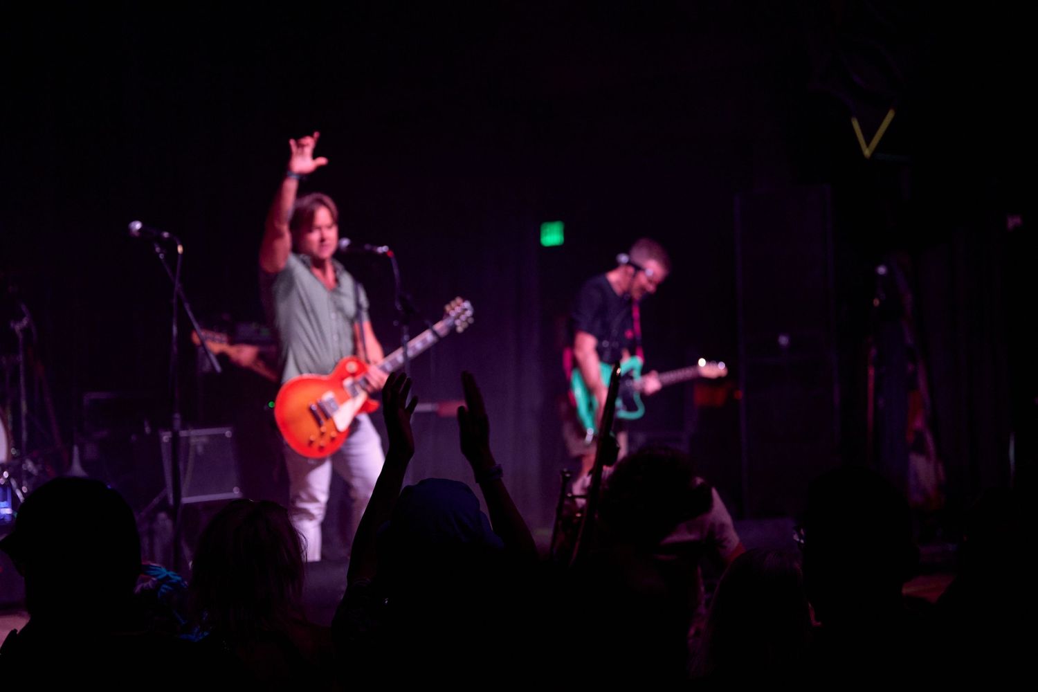 Guitarist performing on stage with raised hand during a live concert