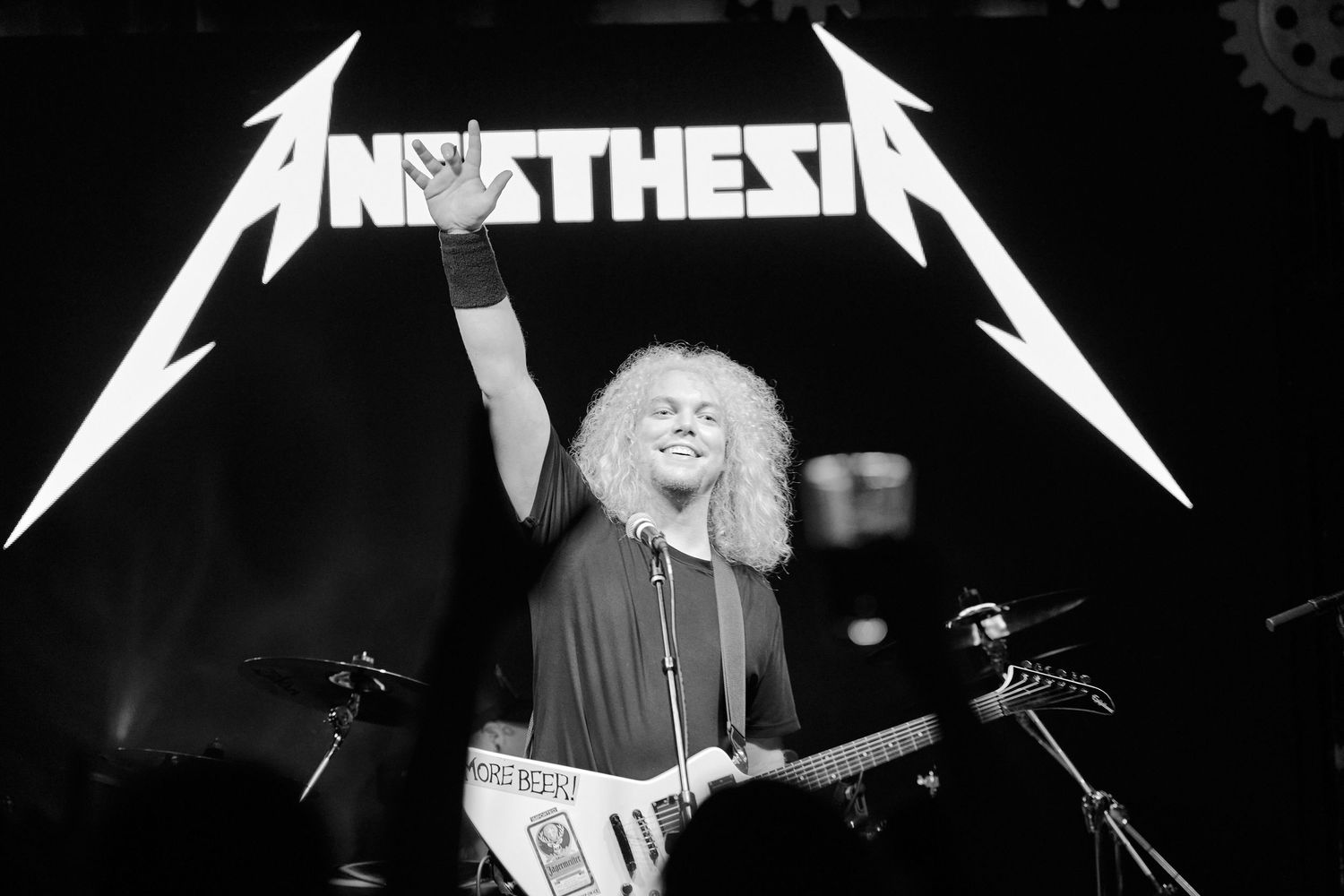 Black and white photo of guitarist performing on stage beneath band signage