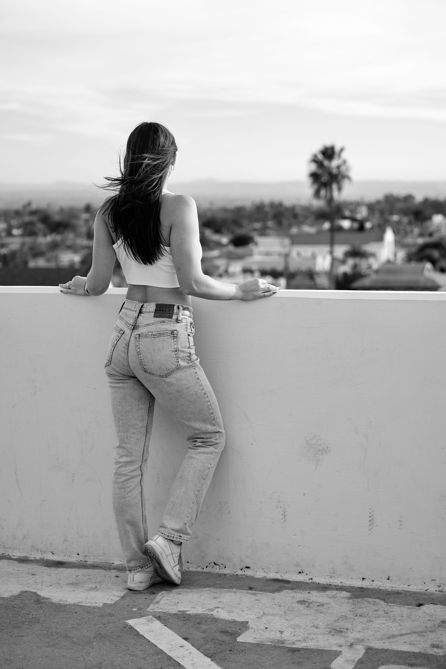 Black and white portrait of woman leaning against a wall overlooking a city