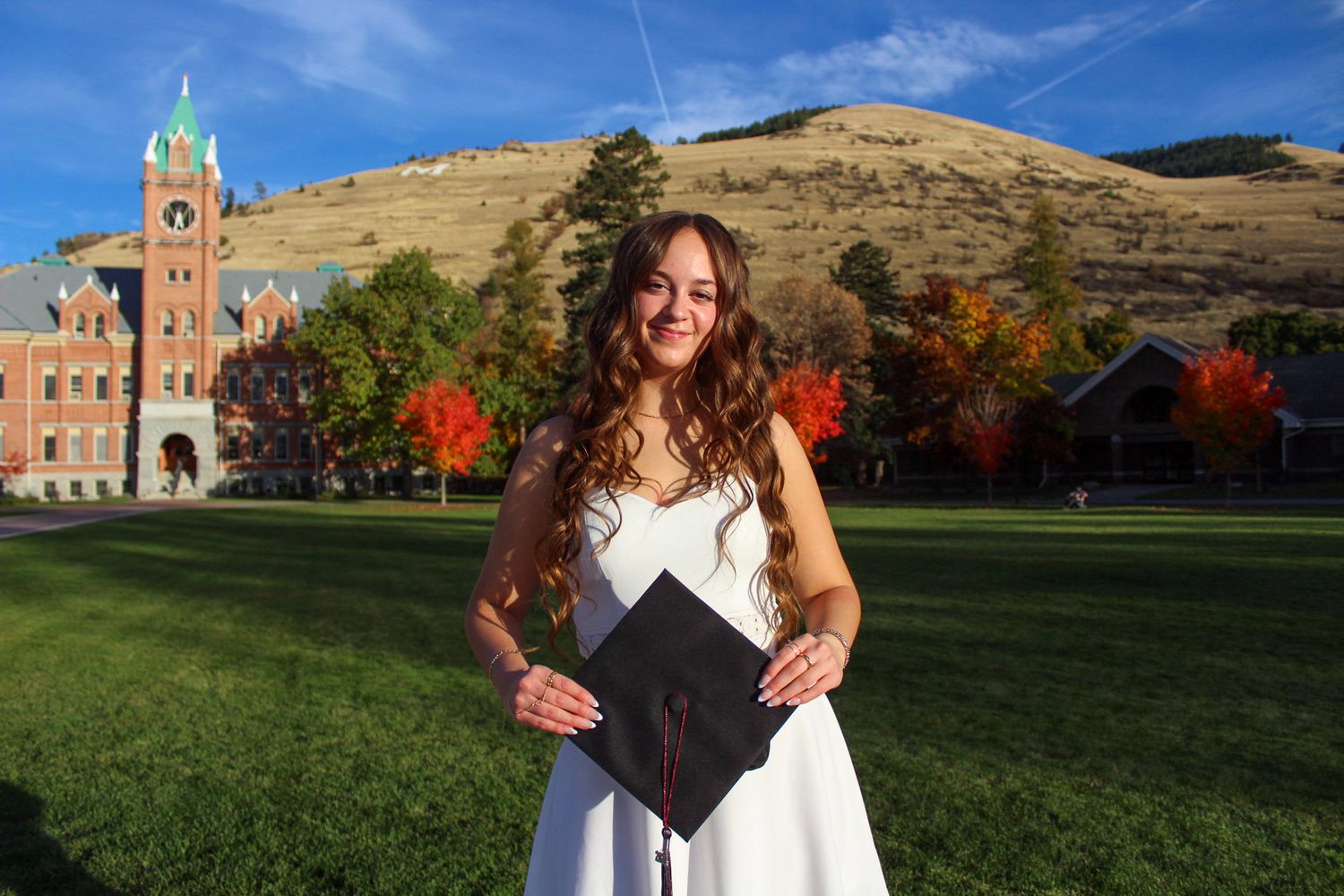A campus quad features fall foliage and historic brick buildings under a bright blue sky at the University of Montana.