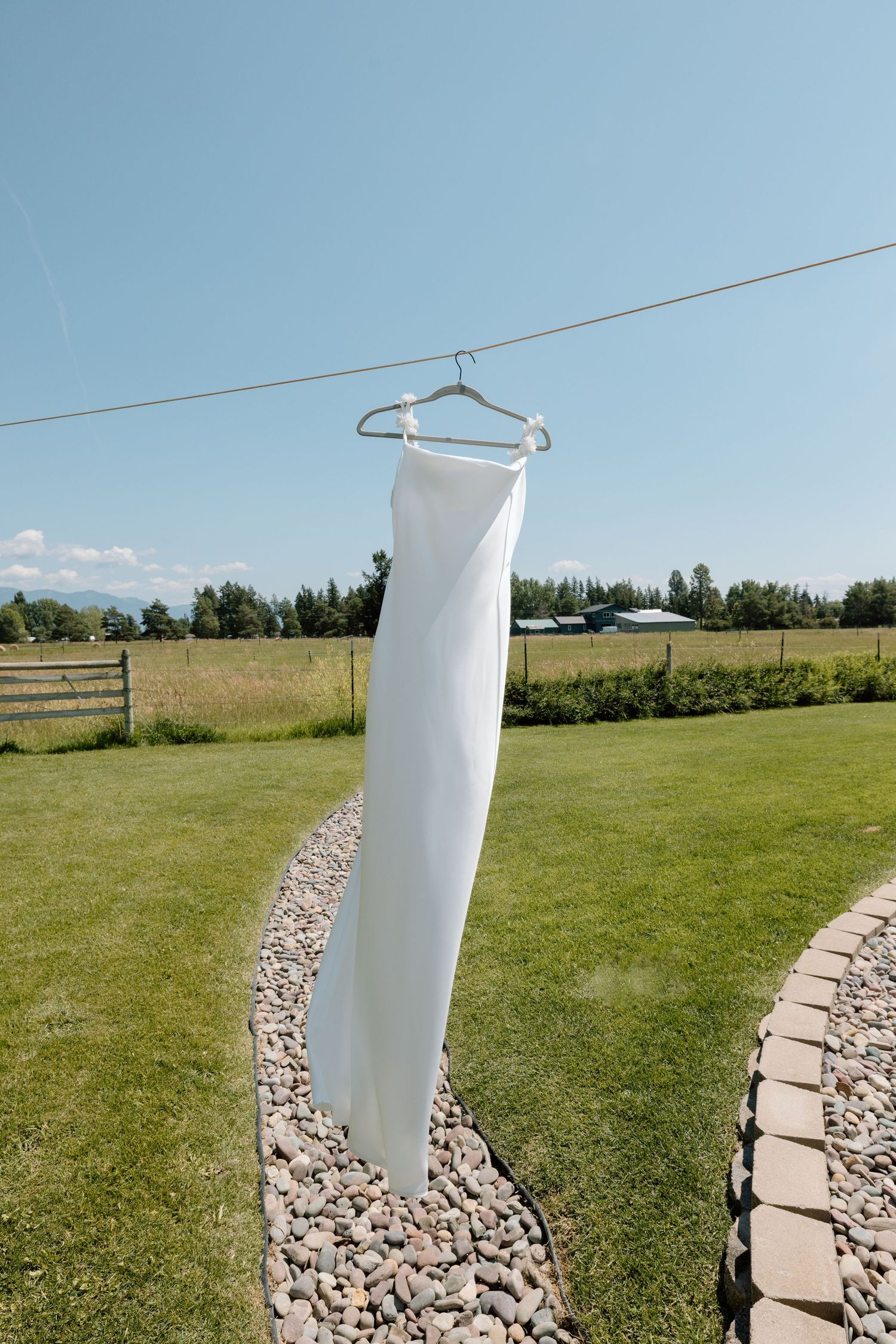 White fabric hanging on clothesline outdoors against blue sky and green grass landscape.