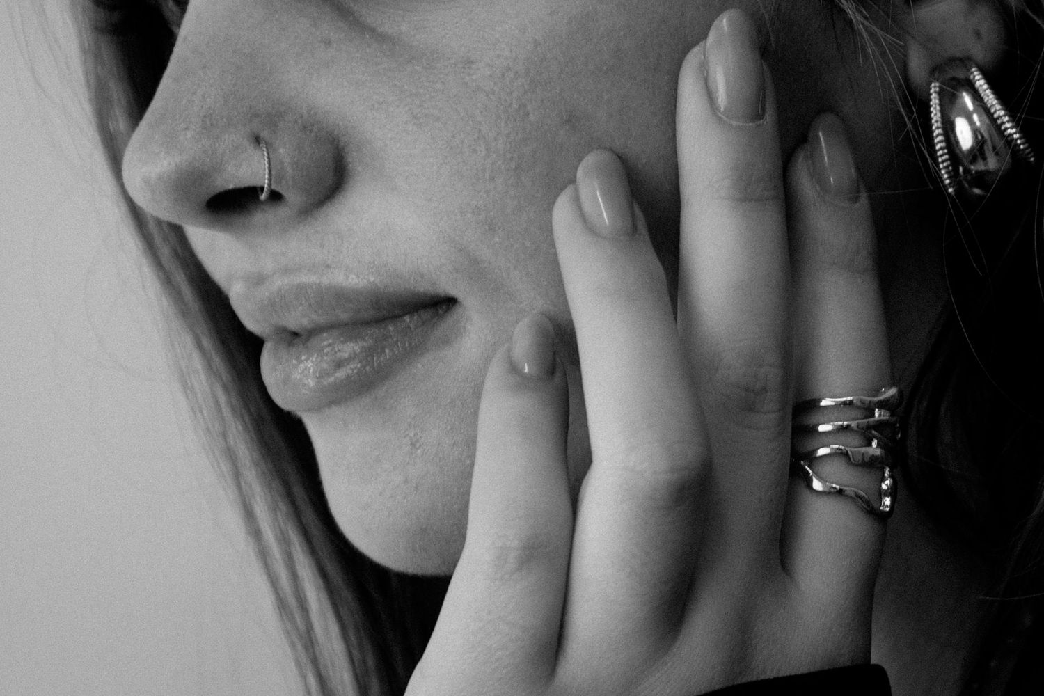 Black and white close-up portrait showing a person's hand resting against their cheek in a contemplative pose.