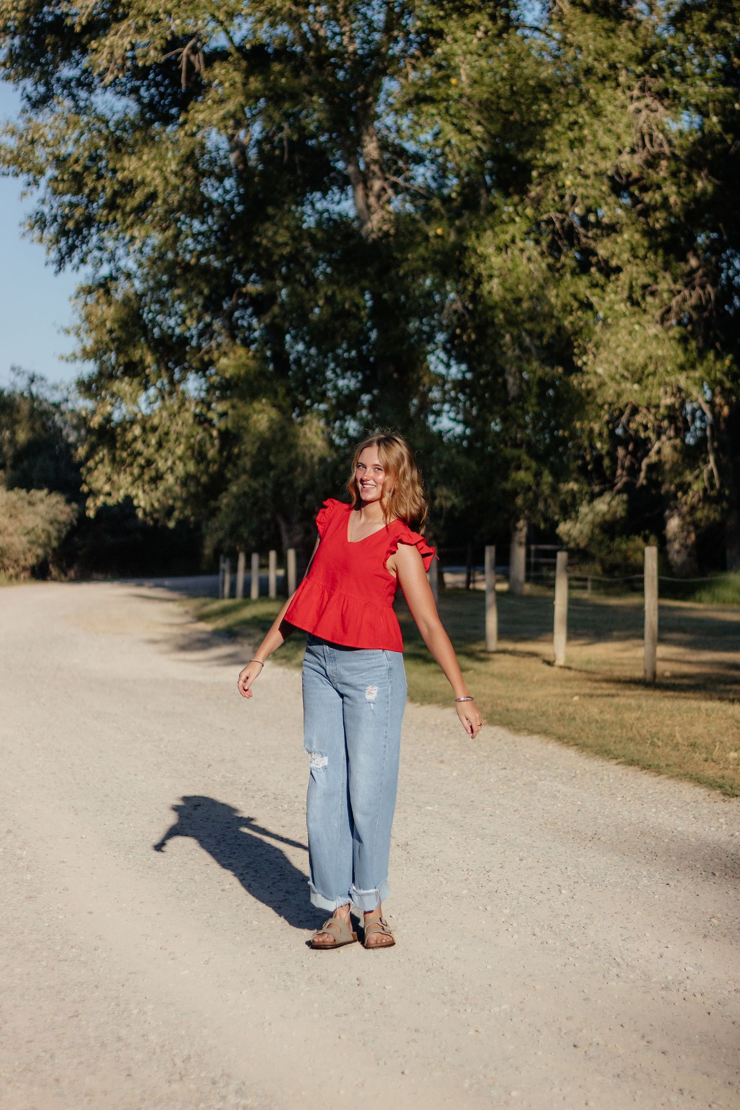 A casual scene on a gravel path shows someone in jeans and red top walking among trees in a park setting.