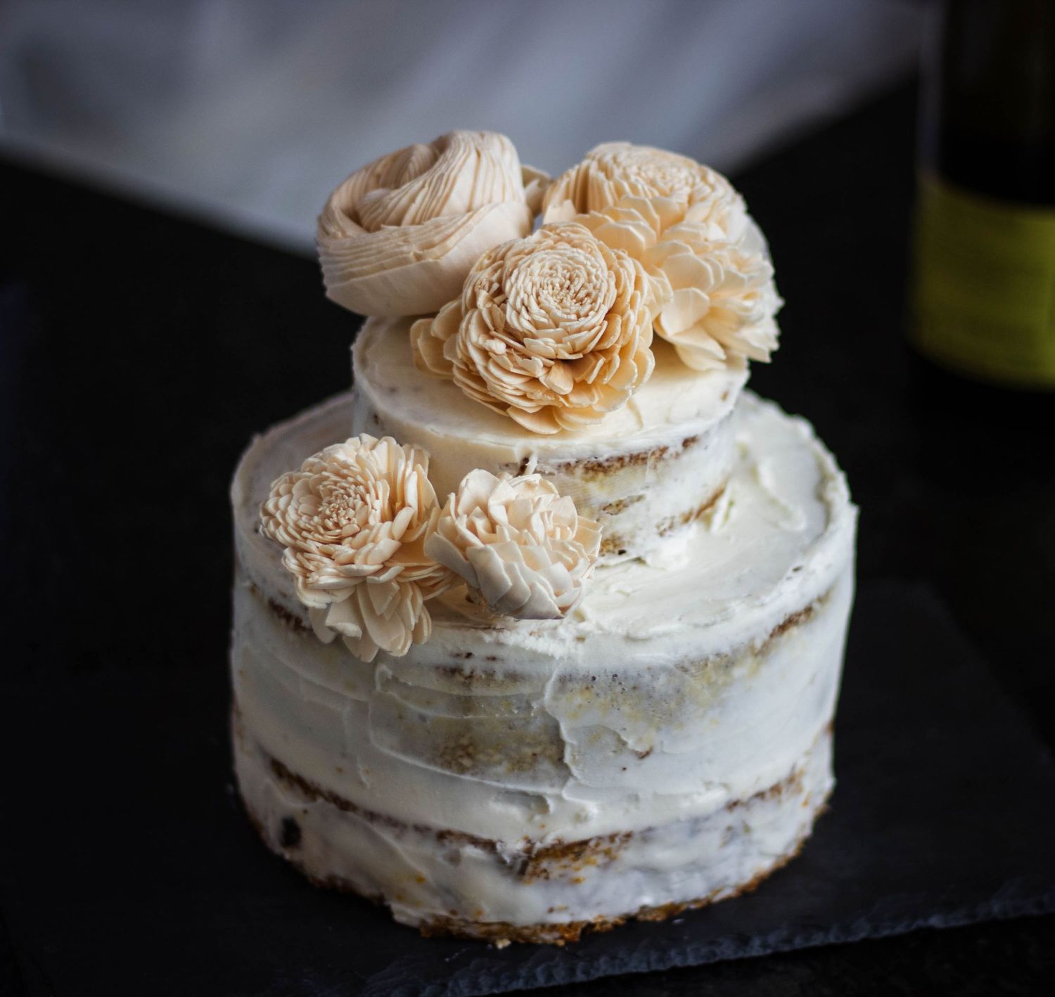A rustic meringue pavlova dessert topped with delicate cream-colored roses arranged in a circular pattern.