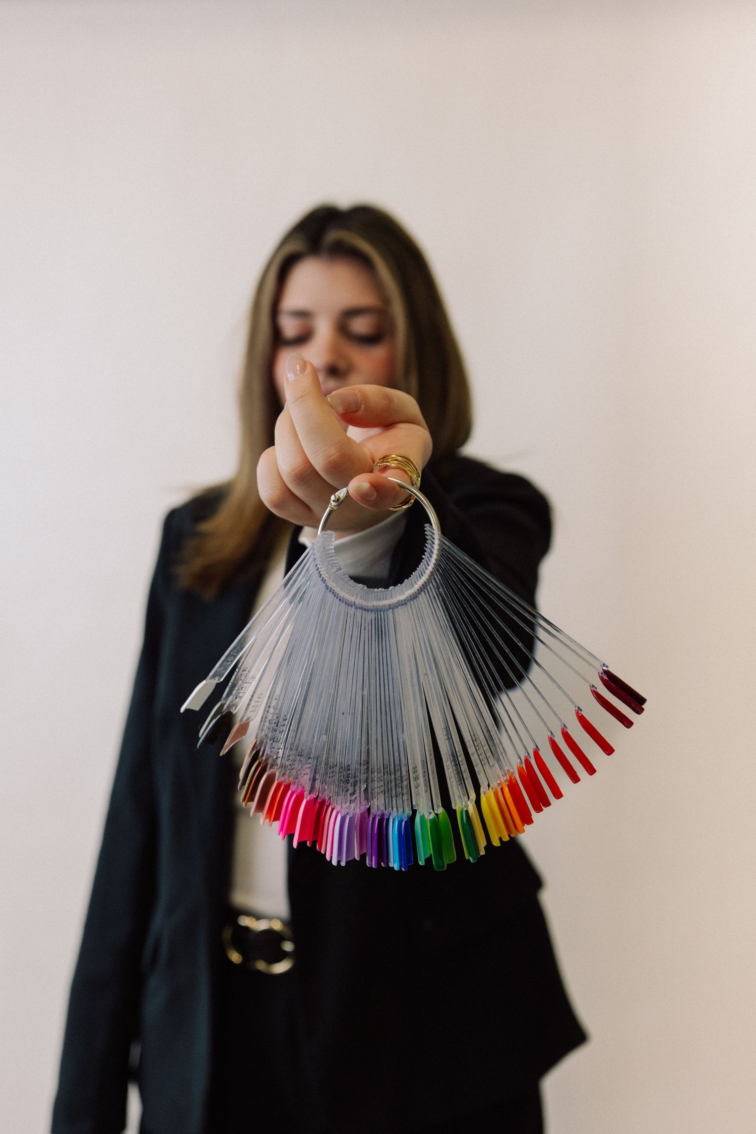 Someone in black holds up a fan-shaped display of colorful nail polish samples against a white background.