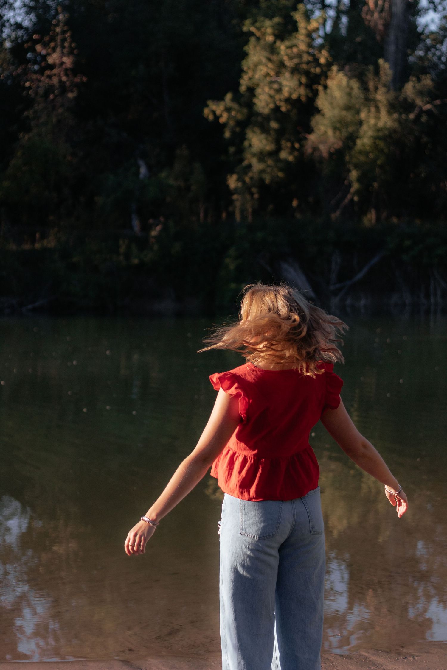 A person in a red shirt and jeans twirls near a lake at sunset creating a dynamic motion sequence.